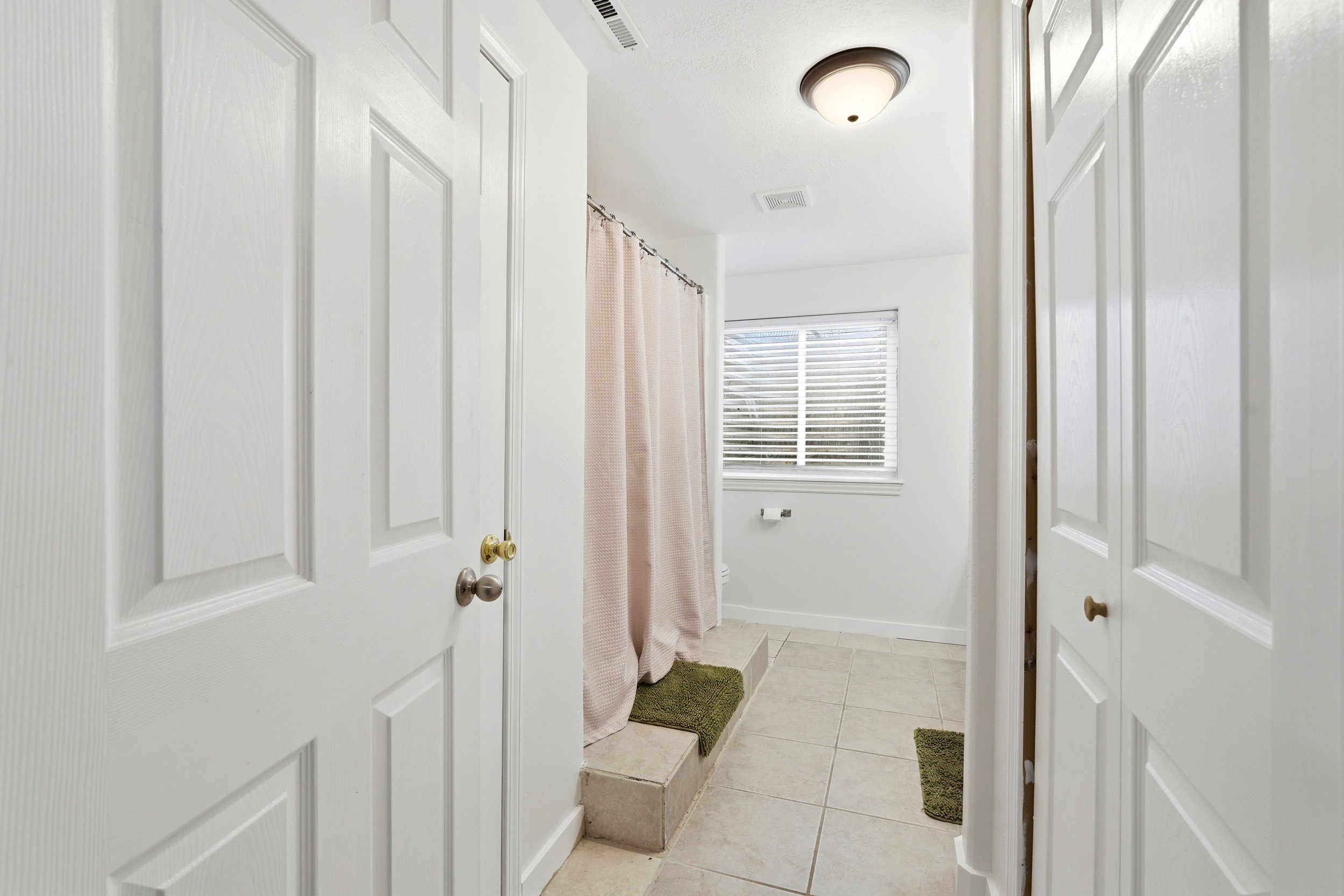 Bathroom featuring neutral tile flooring, a window with horizontal blinds, and a built-in tub surround with a shower curtain
