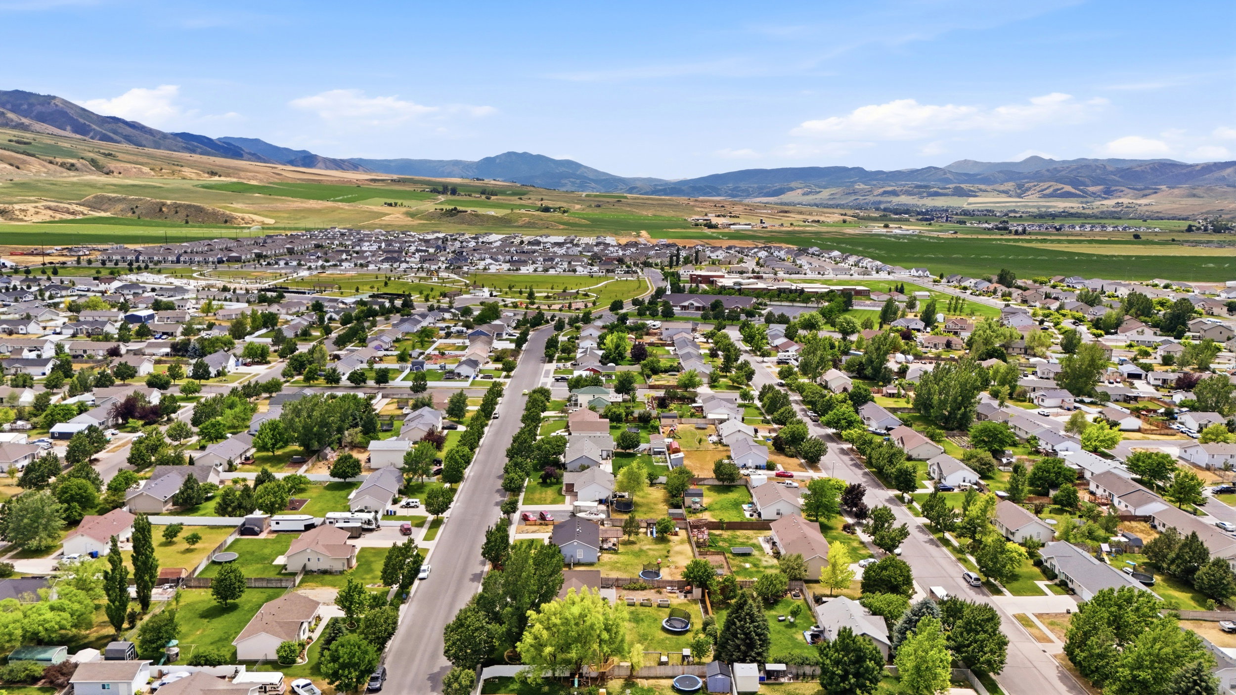 Expansive aerial perspective showcasing a residential development with numerous single-family homes, mature trees, and paved streets