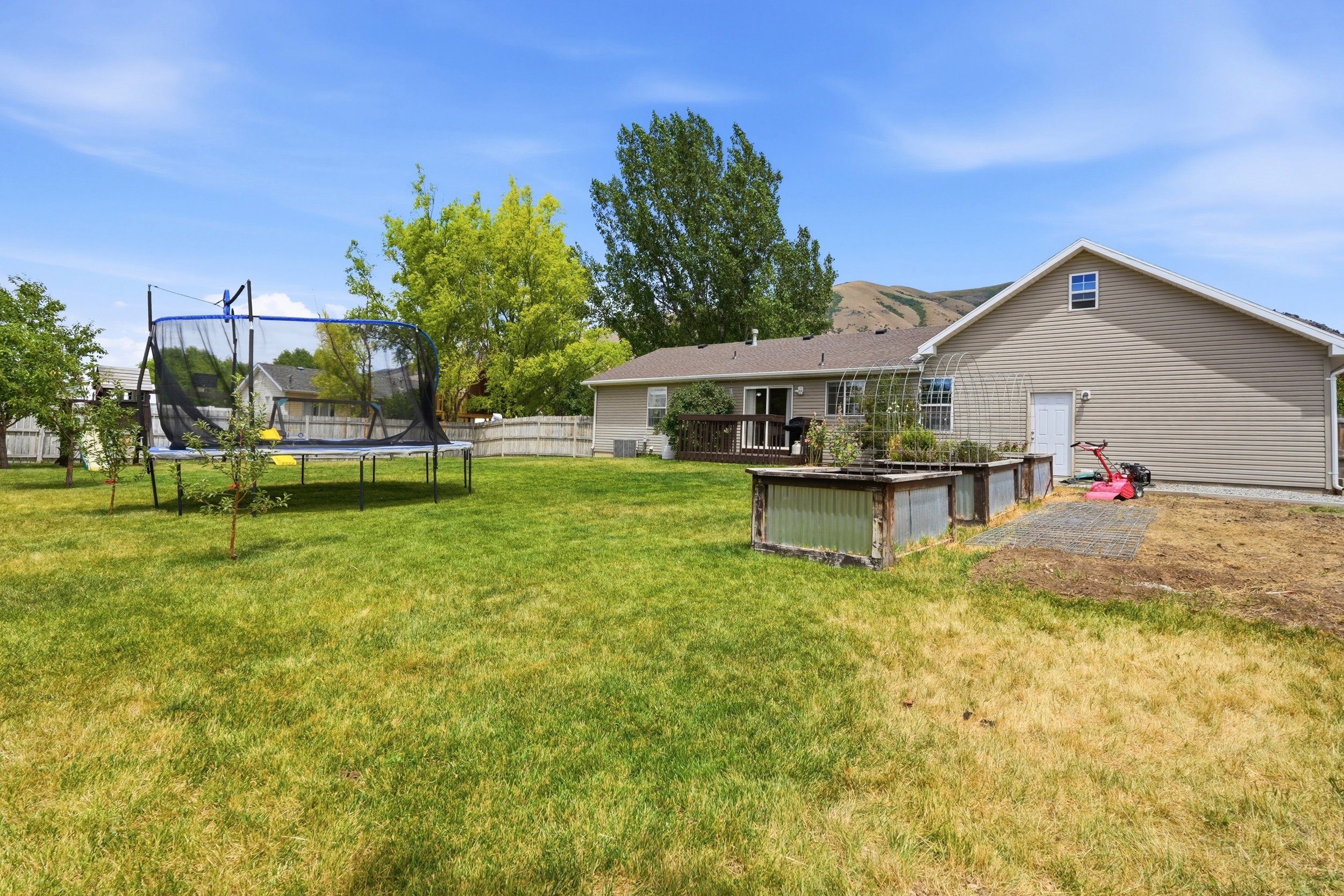 Expansive backyard featuring a green lawn, two raised garden beds with clear panel sides, and a rear deck with a sliding glass door