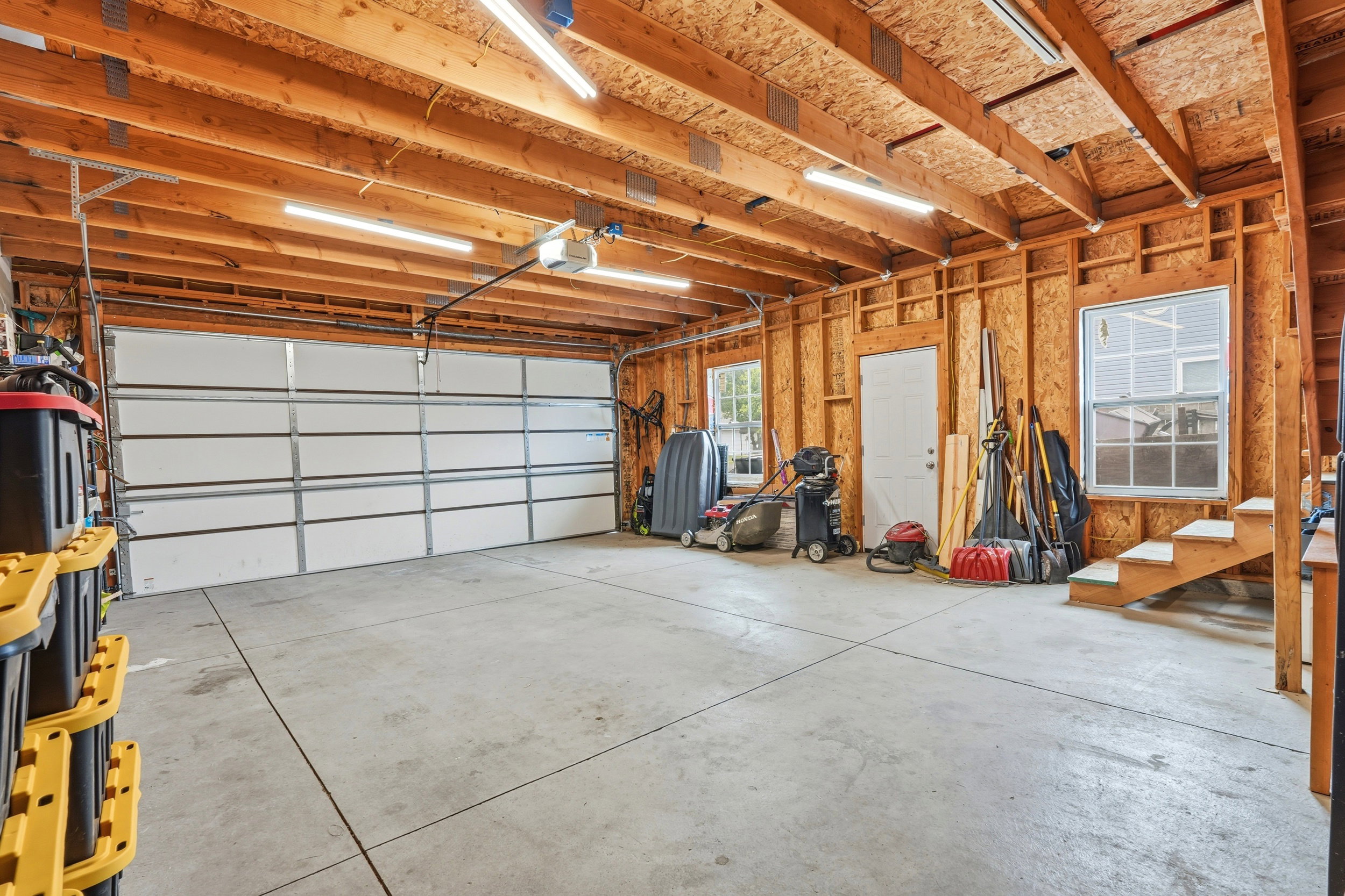 Spacious garage with exposed wood beam ceiling, concrete flooring, and an overhead garage door