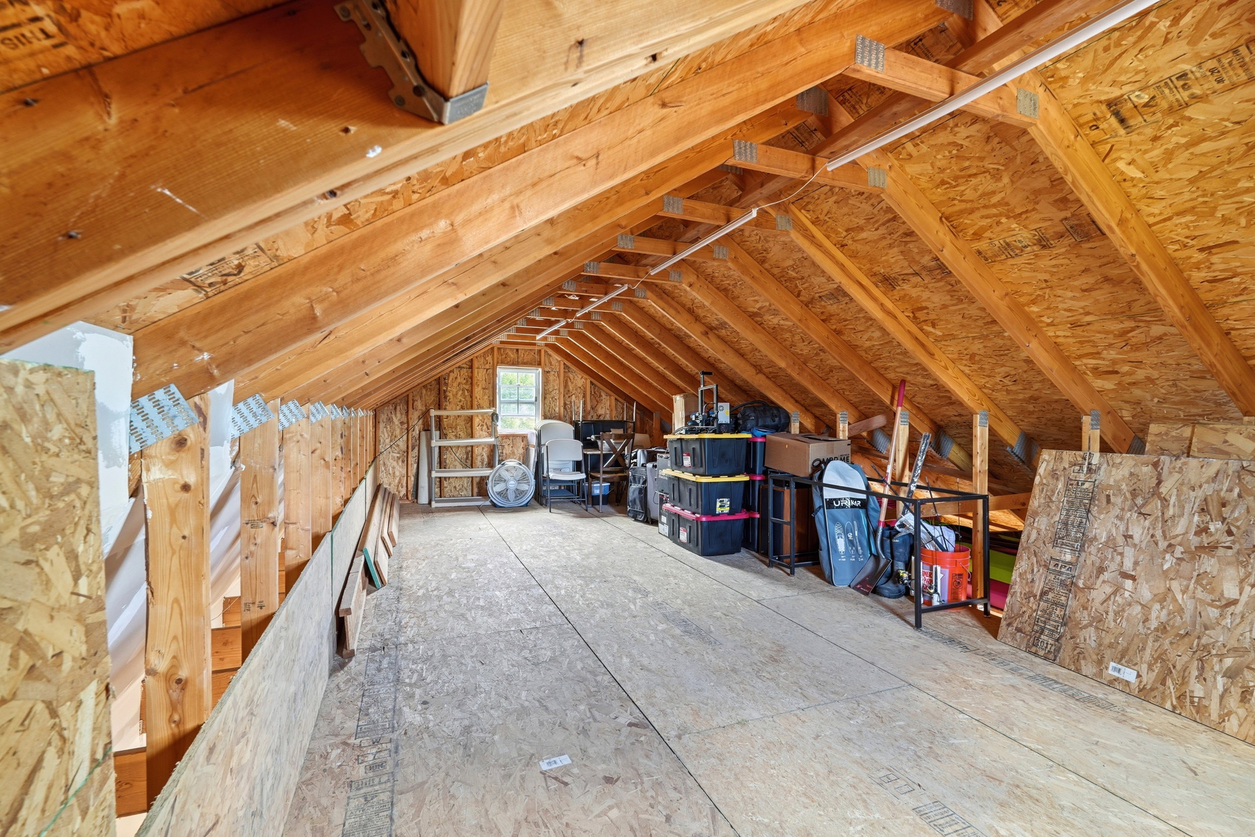 Spacious attic with exposed wood framing, oriented strand board (OSB) flooring, and a single window providing natural light
