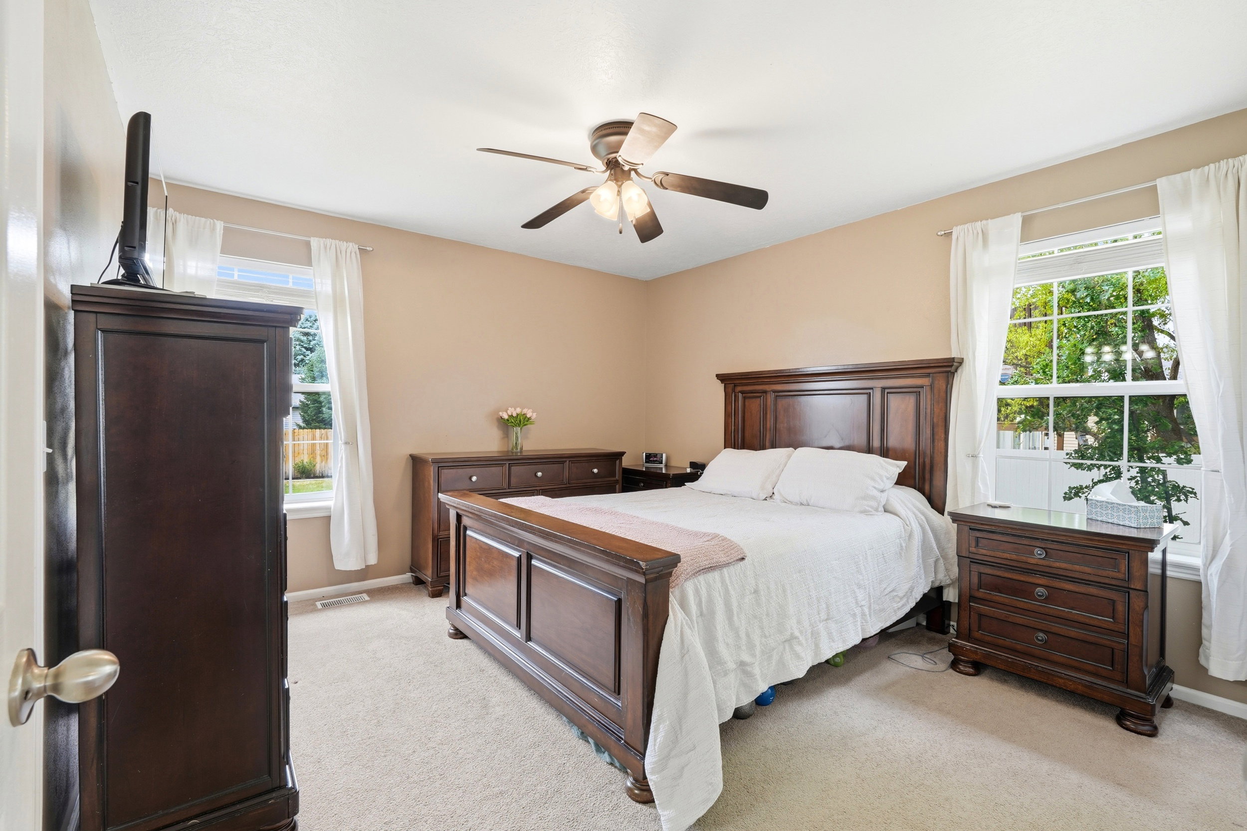 Carpeted room featuring a ceiling fan with light fixture, multiple windows with white trim, and neutral-toned walls