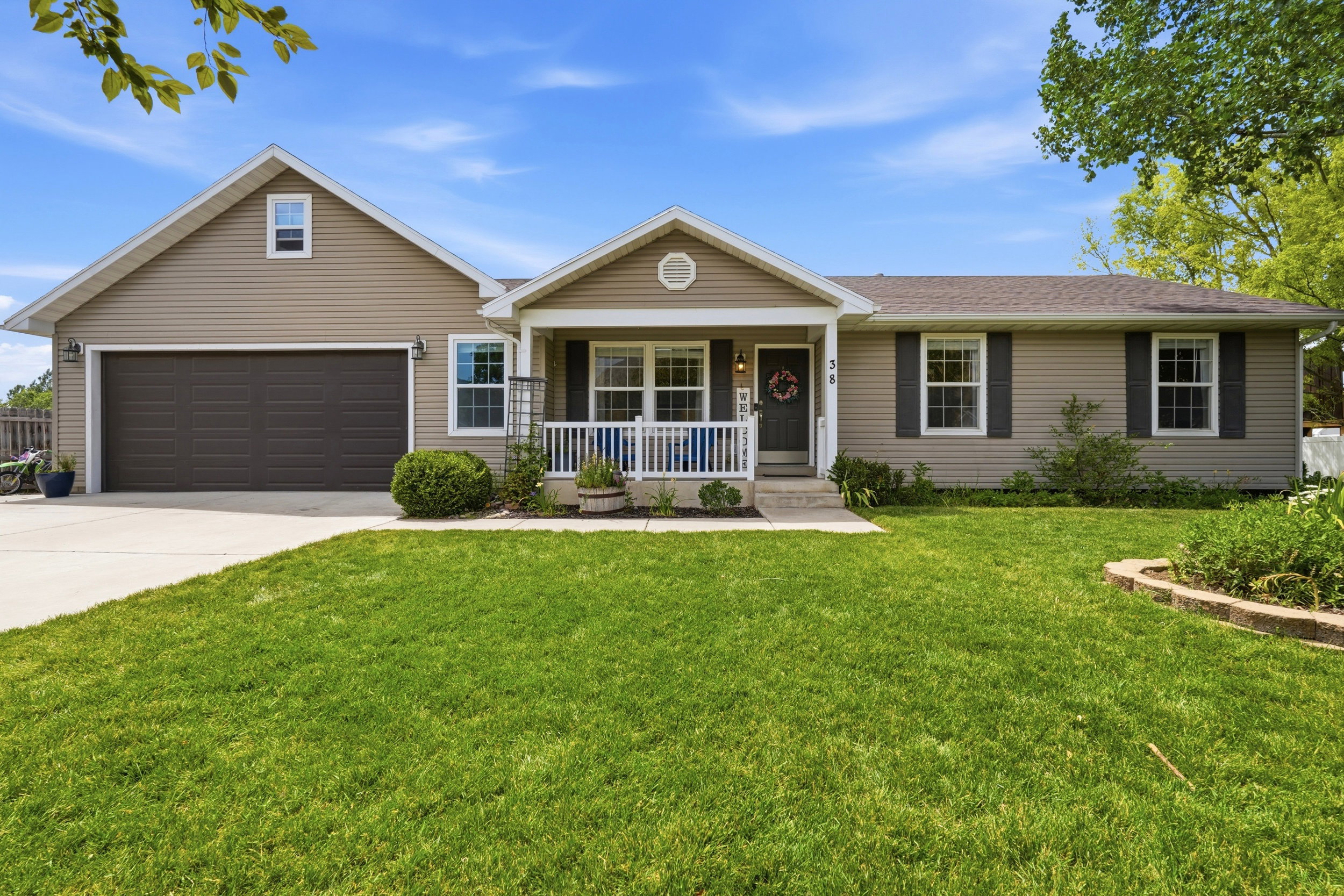 Siding exterior featuring a covered porch, attached garage, concrete driveway, and a front yard with a stone-edged planter