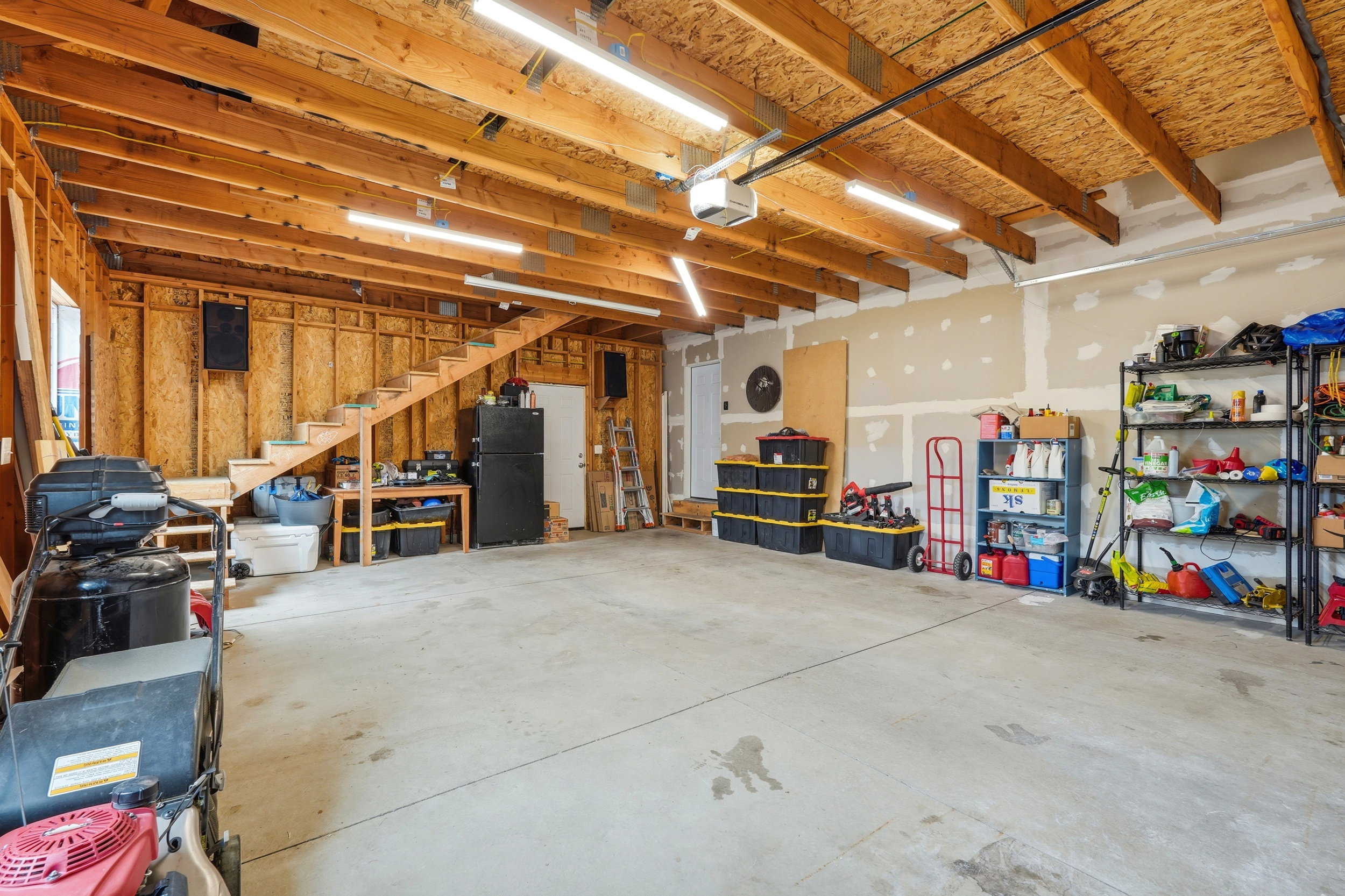 Spacious garage featuring a concrete floor, exposed wood ceiling beams, and ample overhead lighting