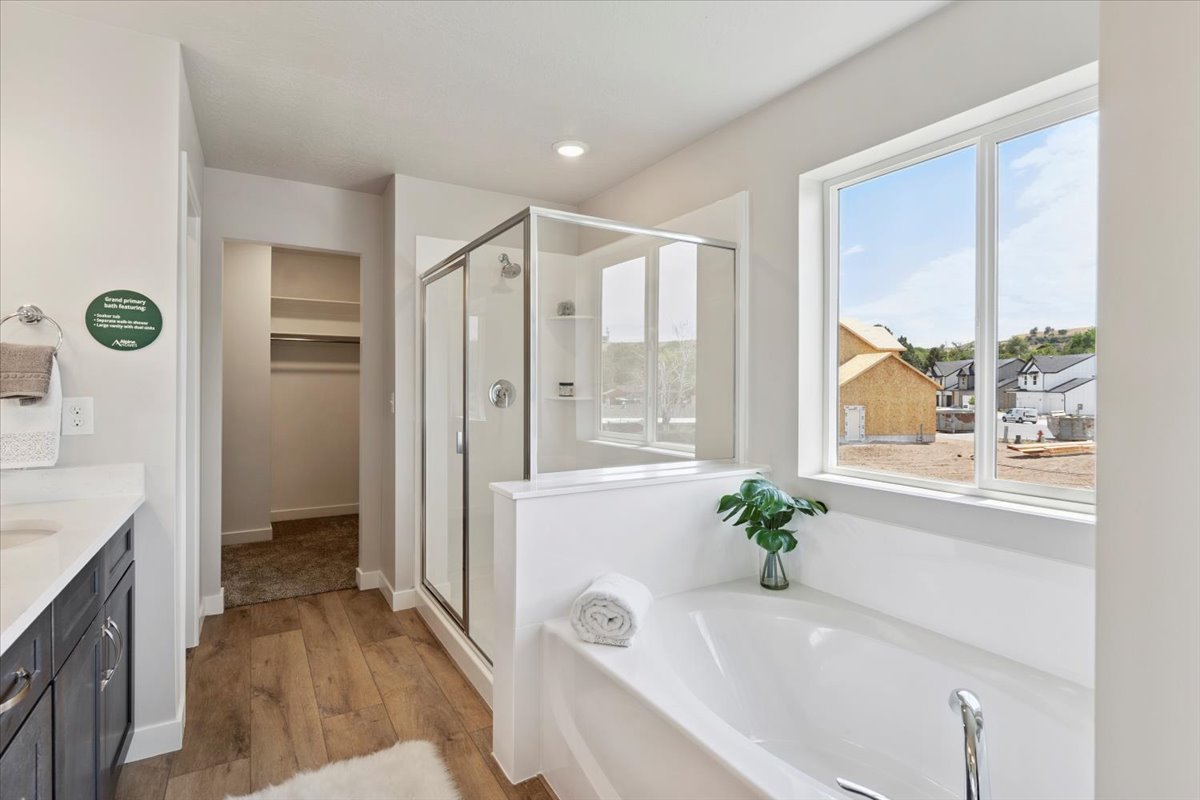 Primary bathroom featuring a built-in soaking tub, glass-enclosed shower, wood-finish flooring, and a large window