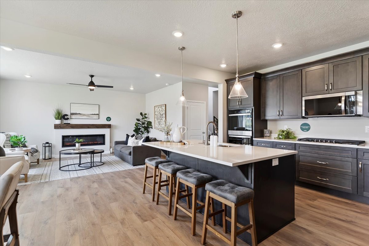 Open-concept living space featuring a spacious kitchen island, dark wood-finish cabinetry, built-in stainless steel appliances, and wood-finish flooring