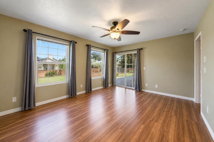 Spacious room featuring wood-finish flooring, light green walls, a ceiling fan with integrated lighting, a sliding glass door, and multiple grid-pattern windows