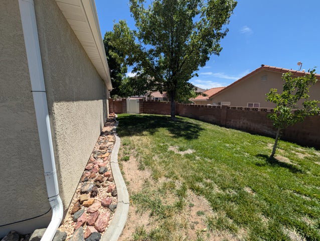 Expansive backyard featuring a concrete block fence, established trees, a storage shed, and a decorative rock border along the house
