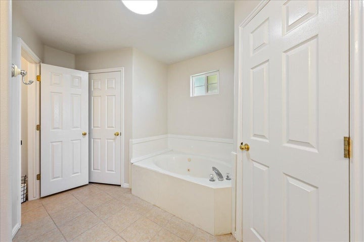 Soaking tub with chrome fixtures, tiled flooring, and a transom window