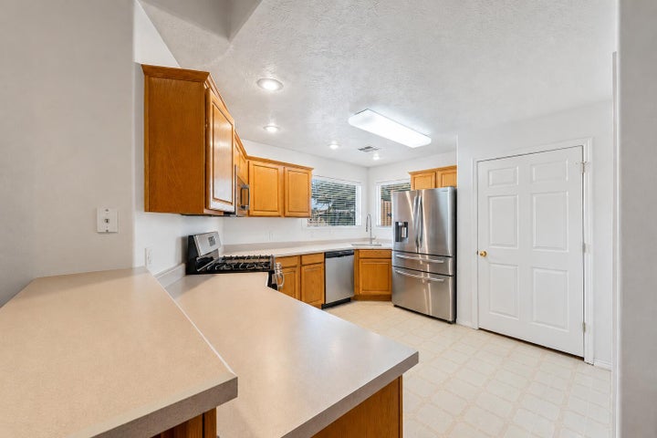 Kitchen featuring wood cabinetry, light-toned countertops, stainless steel appliances, and patterned tile flooring