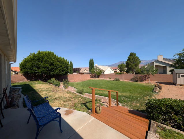 Expansive backyard featuring a large grass area, concrete patio, and a wood-finish deck