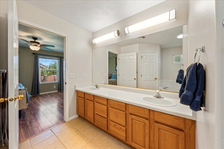 Bathroom vanity with dual sinks, wood-finish cabinetry, and a full-width mirror