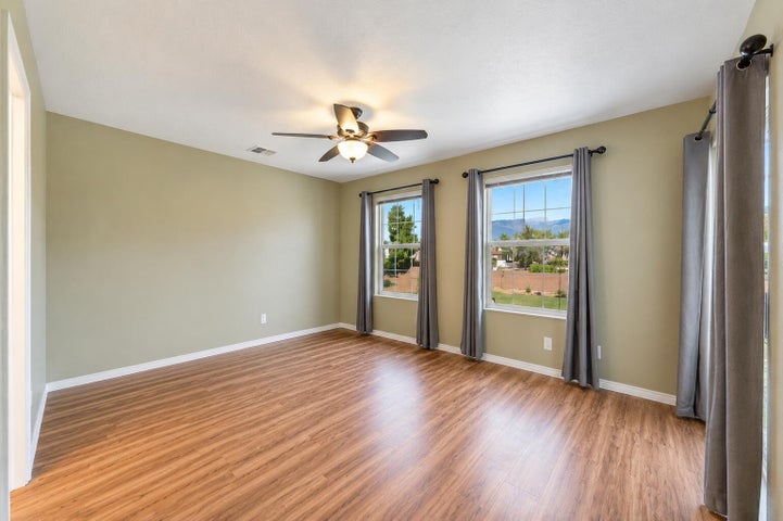 Spacious room featuring wood-finish flooring, two large windows, a ceiling fan with integrated lighting, and neutral wall tones