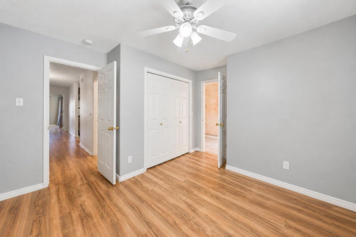 Bedroom featuring wood-finish flooring, light gray walls, a white ceiling fan with integrated lighting, white baseboards, and a bi-fold closet door