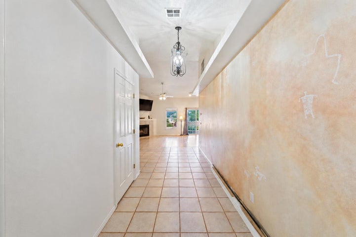 Long hallway with tile flooring, a decorative overhead light fixture, and a textured accent wall