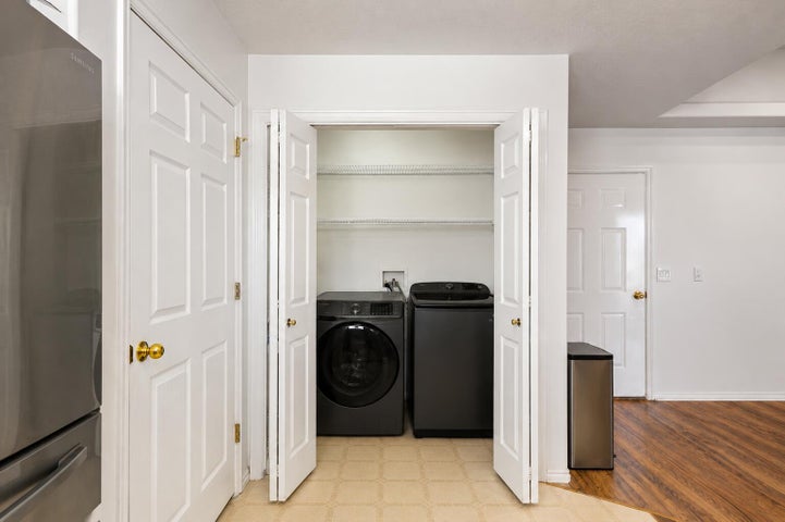 Dedicated laundry closet with bi-fold doors, equipped with a front-loading washing machine and top-loading dryer, and overhead wire shelving