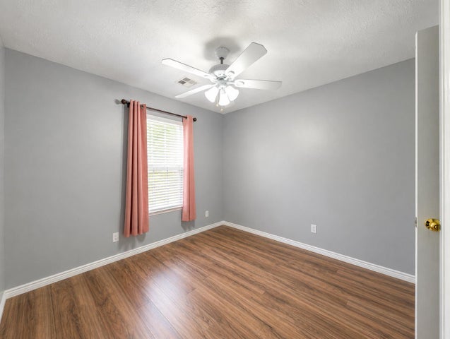 Spacious room featuring wood-finish flooring, light grey walls, and a white ceiling fan with integrated lighting