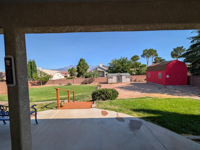 Expansive backyard featuring a concrete patio, a small wooden deck, a red barn-style shed, and a second storage shed