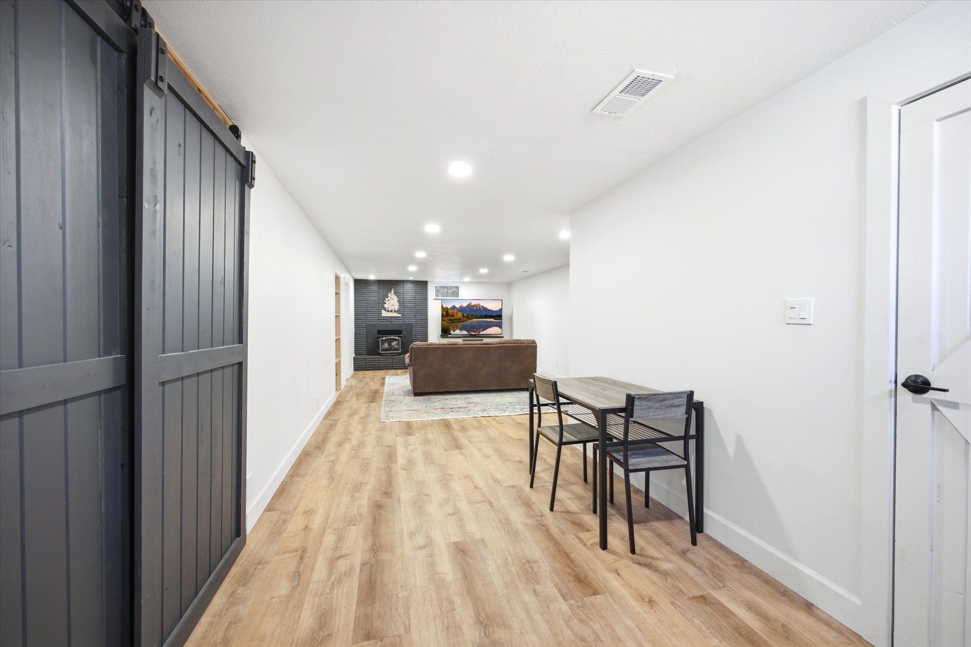 Spacious lower-level area with wood-finish flooring, recessed lighting, and a dark sliding barn door