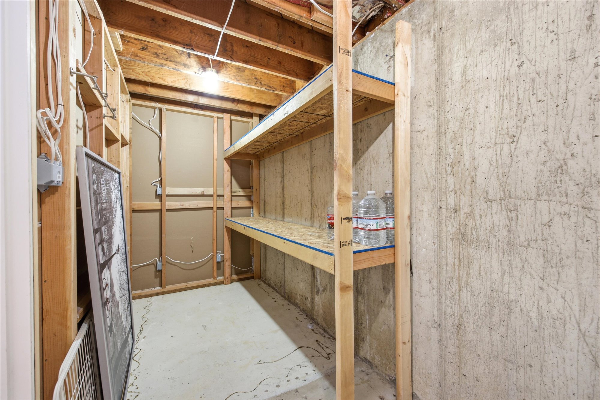 Unfinished basement area featuring exposed wood framing, concrete floor, and built-in wood shelving for storage for cold storage