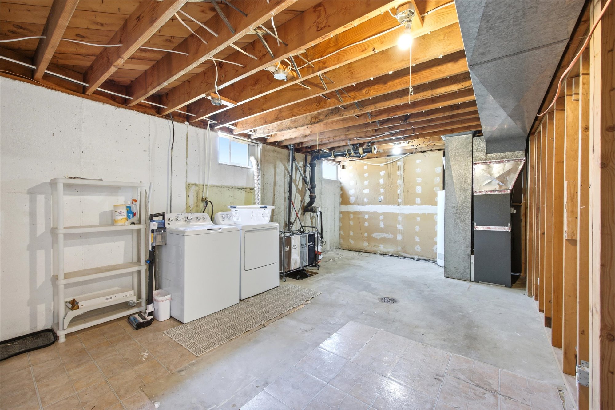 Unfinished lower level featuring exposed wood joists, concrete flooring, and a laundry area with appliances.  Large room that has space for new ideas for uses.