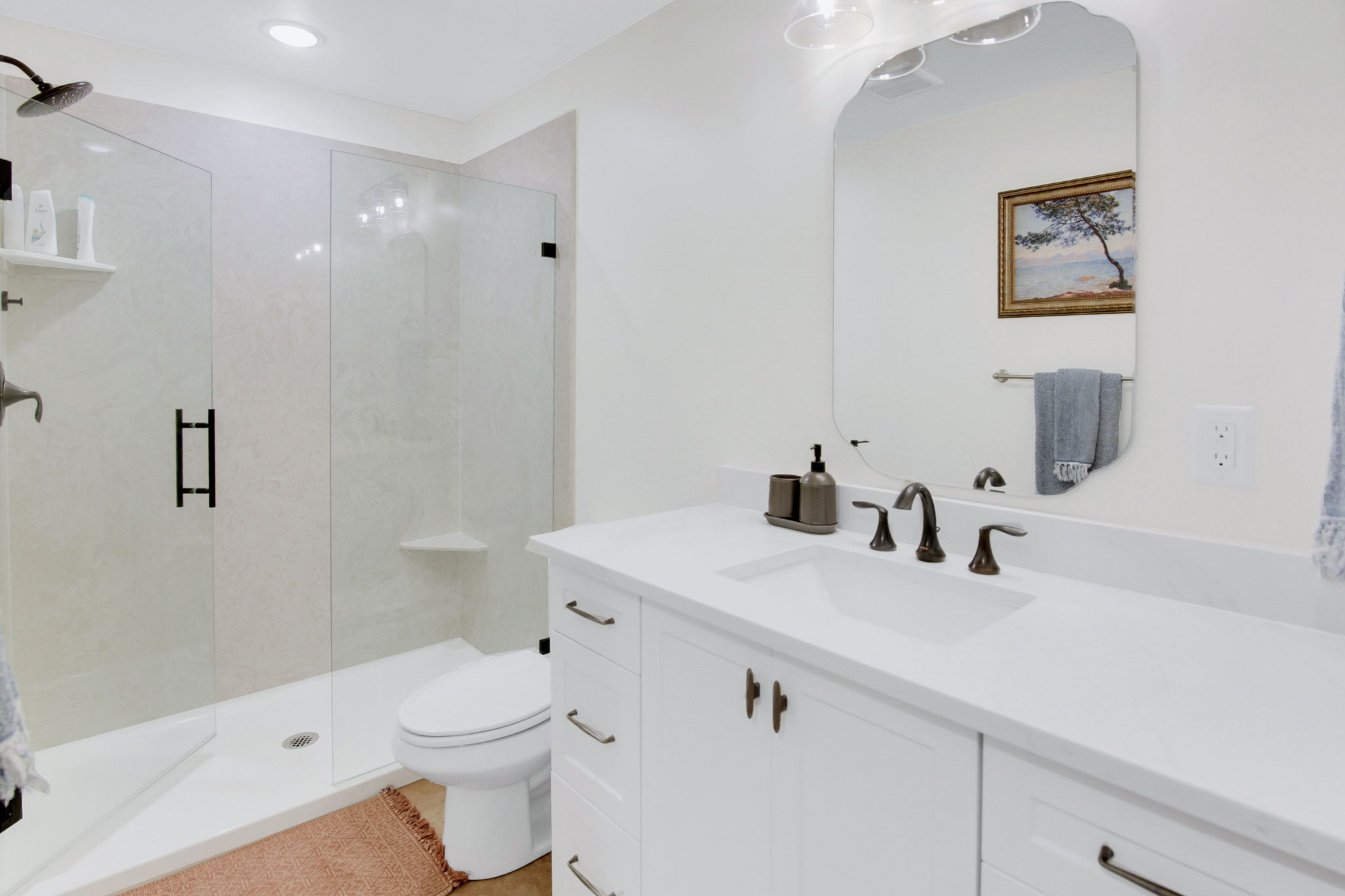 Bathroom featuring a glass-enclosed shower with a black rain shower head, white tiled walls, and a built-in corner shelf