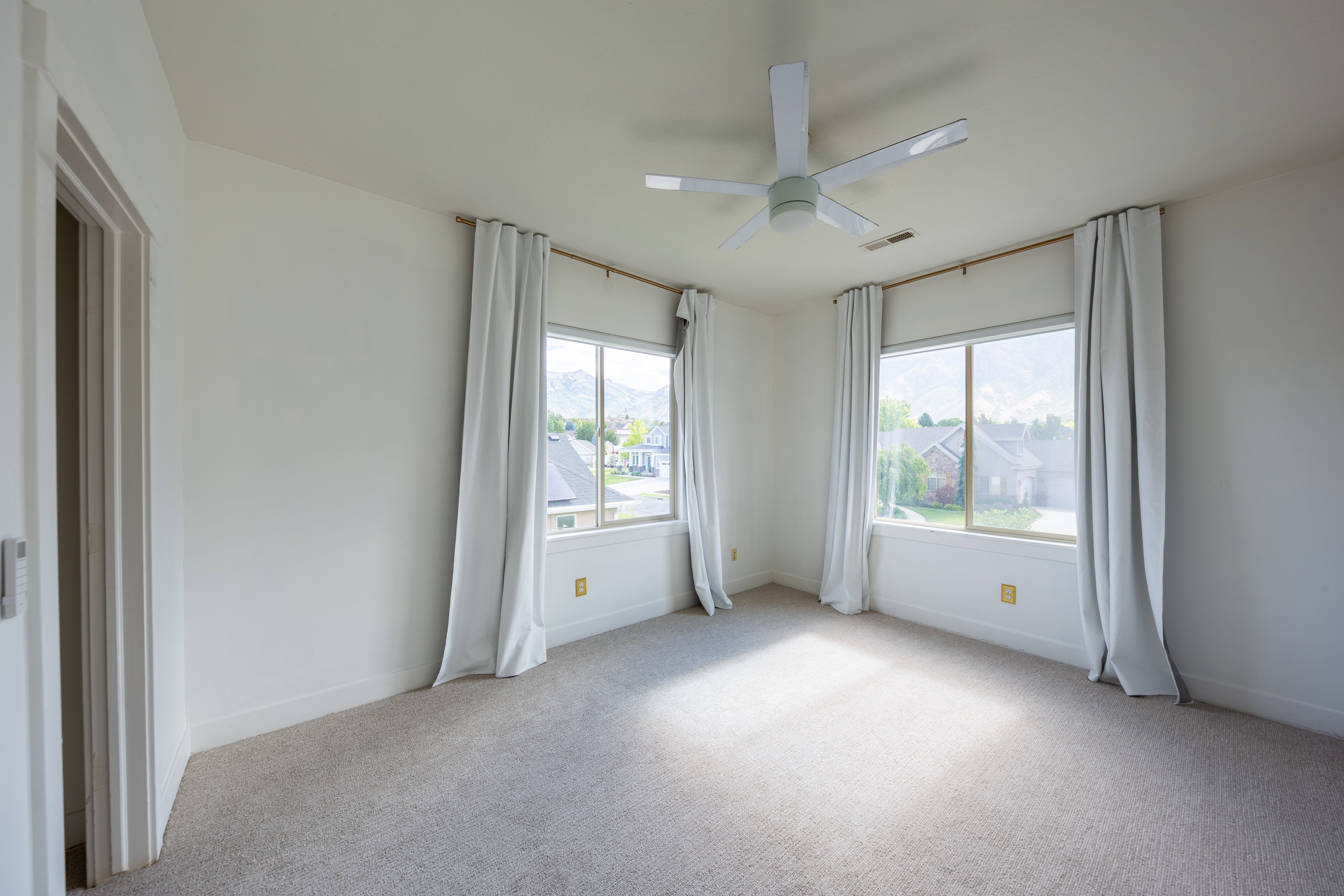 Bright room featuring two large windows, a ceiling fan, and light-toned carpeting