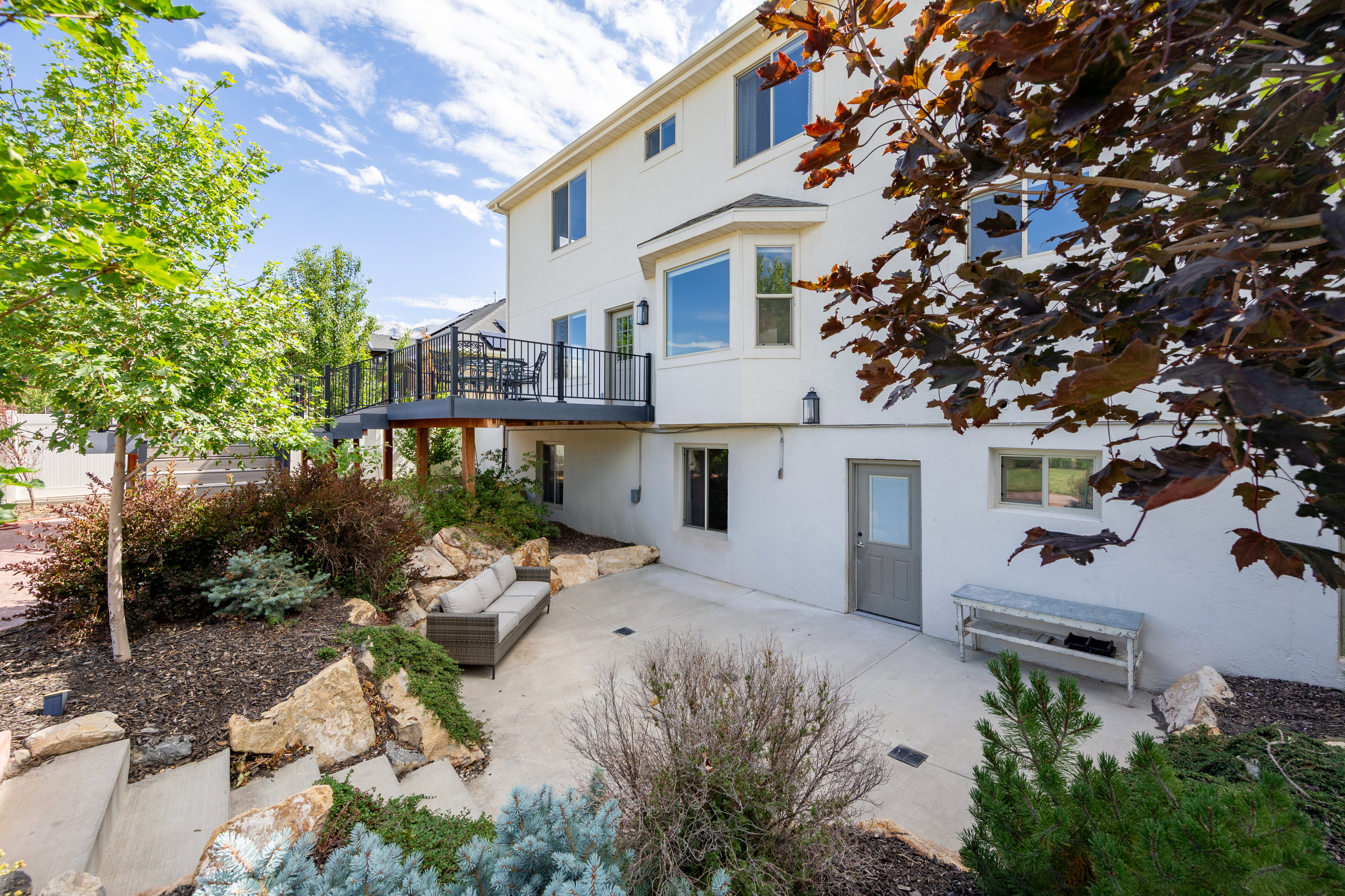 Rear exterior featuring a raised deck with black railings, a ground-level concrete patio, and a bay window