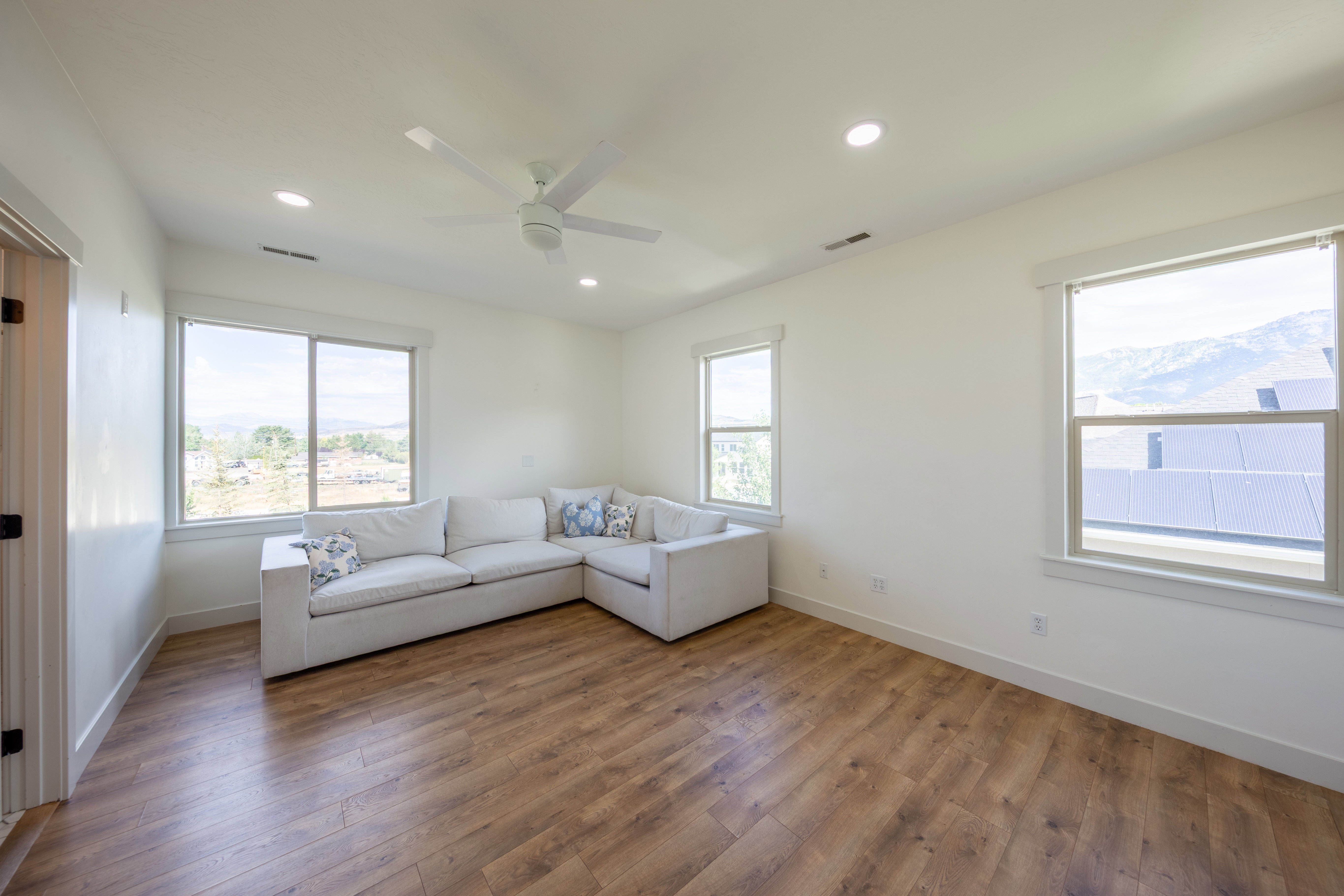 Spacious room featuring wood-finish flooring, ample natural light from multiple windows, recessed lighting, and a ceiling fan