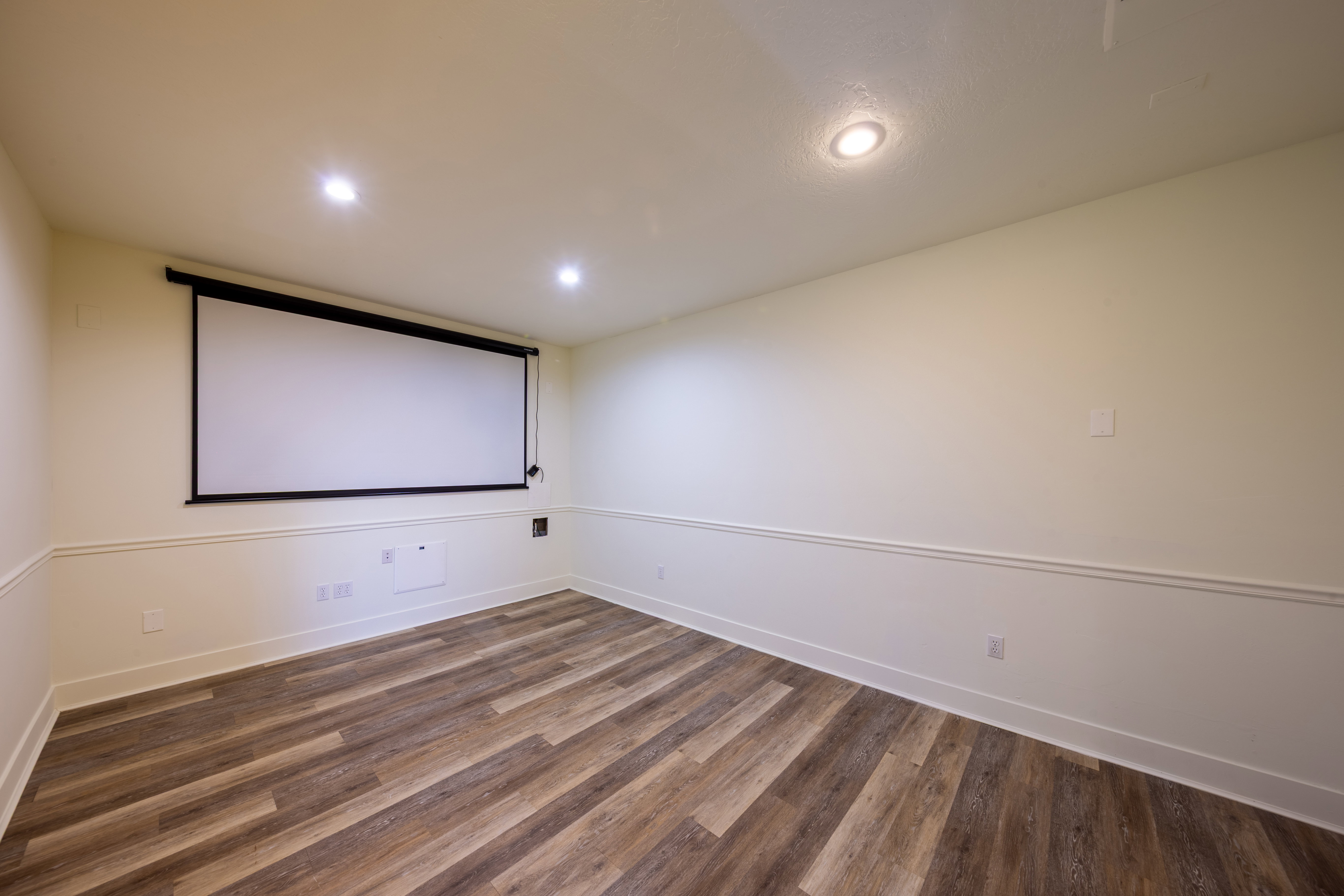 Spacious room featuring a retractable projection screen, recessed lighting, wood-finish flooring, and two-tone walls with chair rail molding