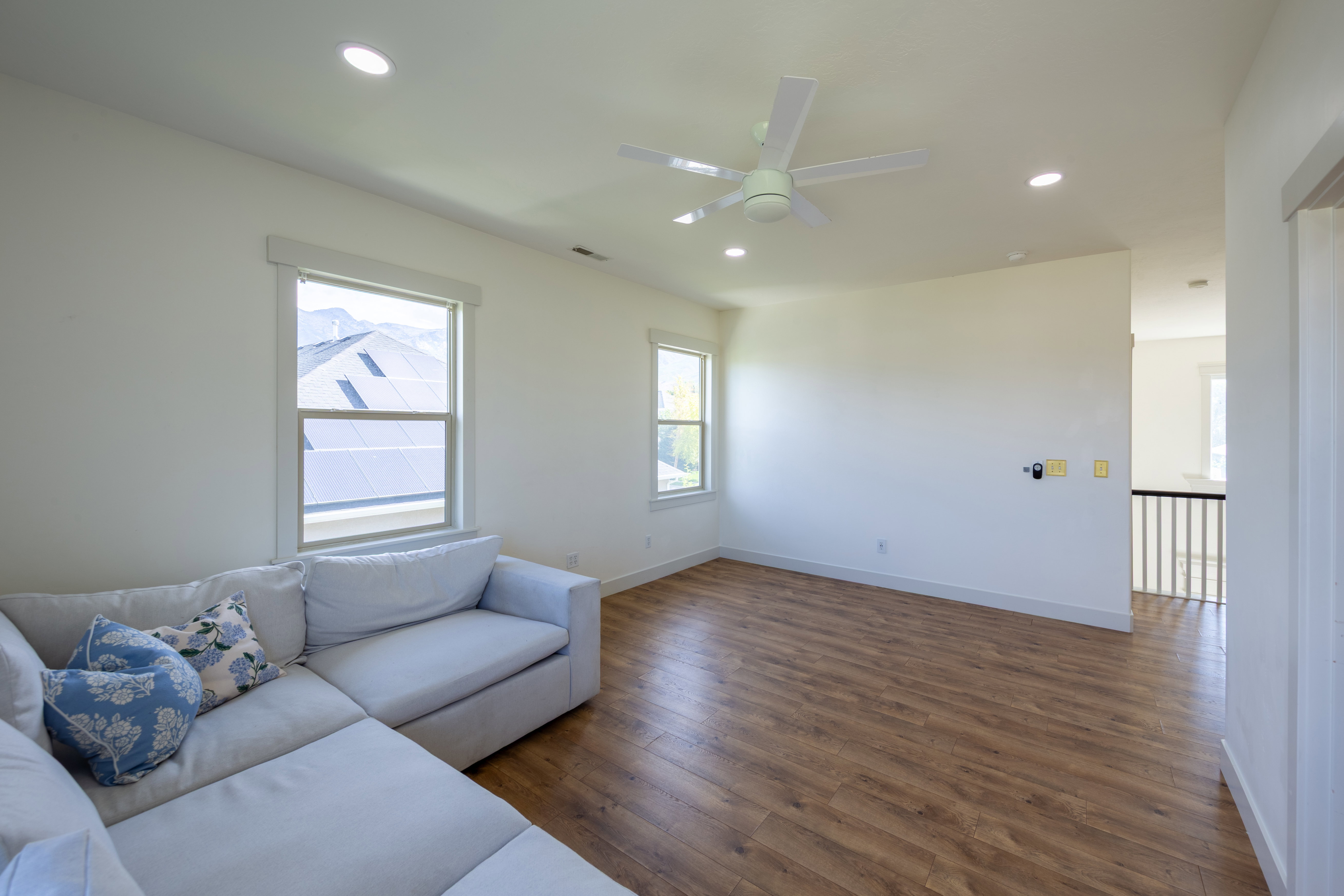 Spacious room featuring wood-finish flooring, ample natural light from multiple windows, a ceiling fan, and recessed lighting