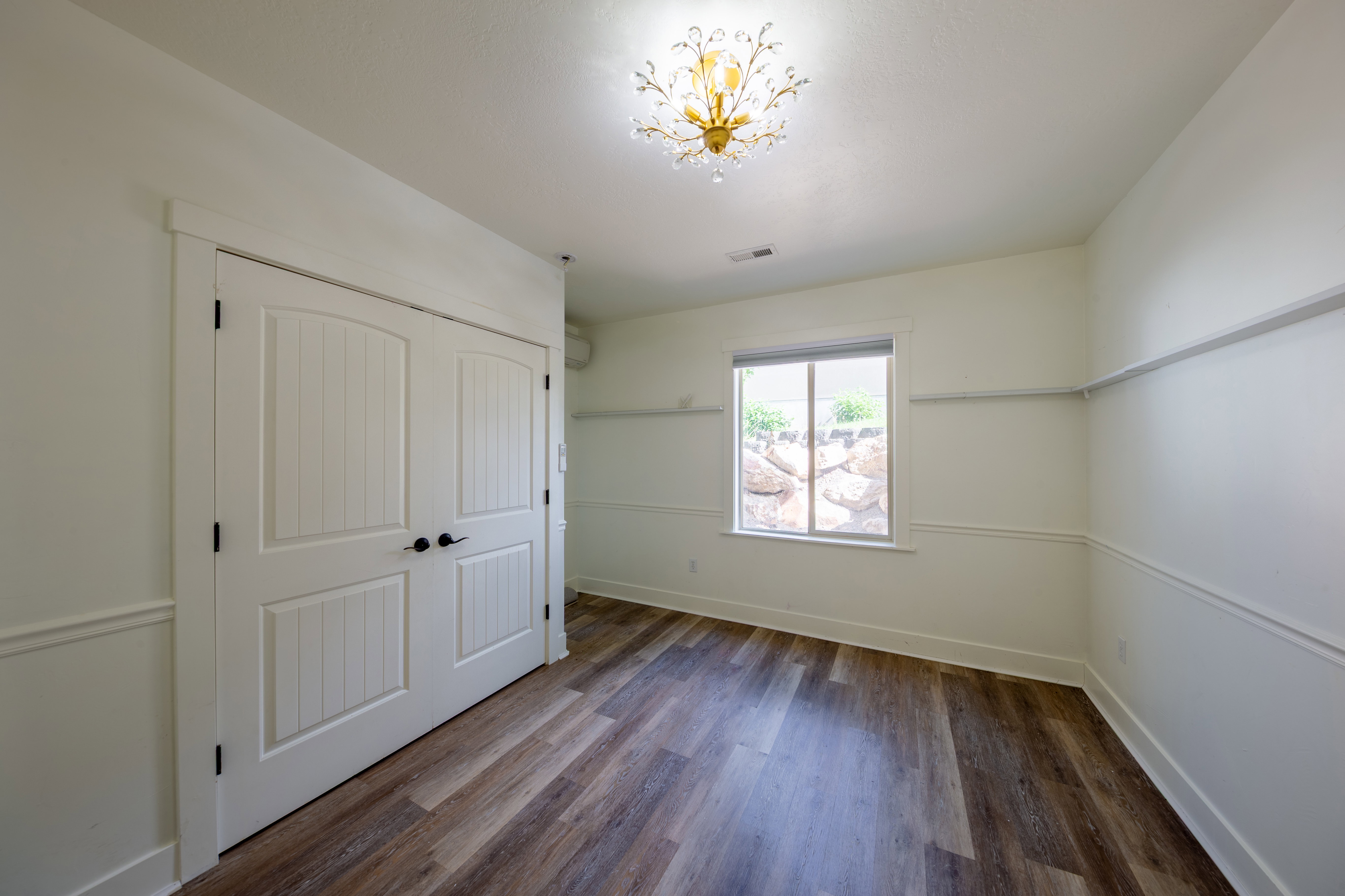 Spacious room featuring wood-finish flooring, white paneled double closet doors, and decorative wainscoting