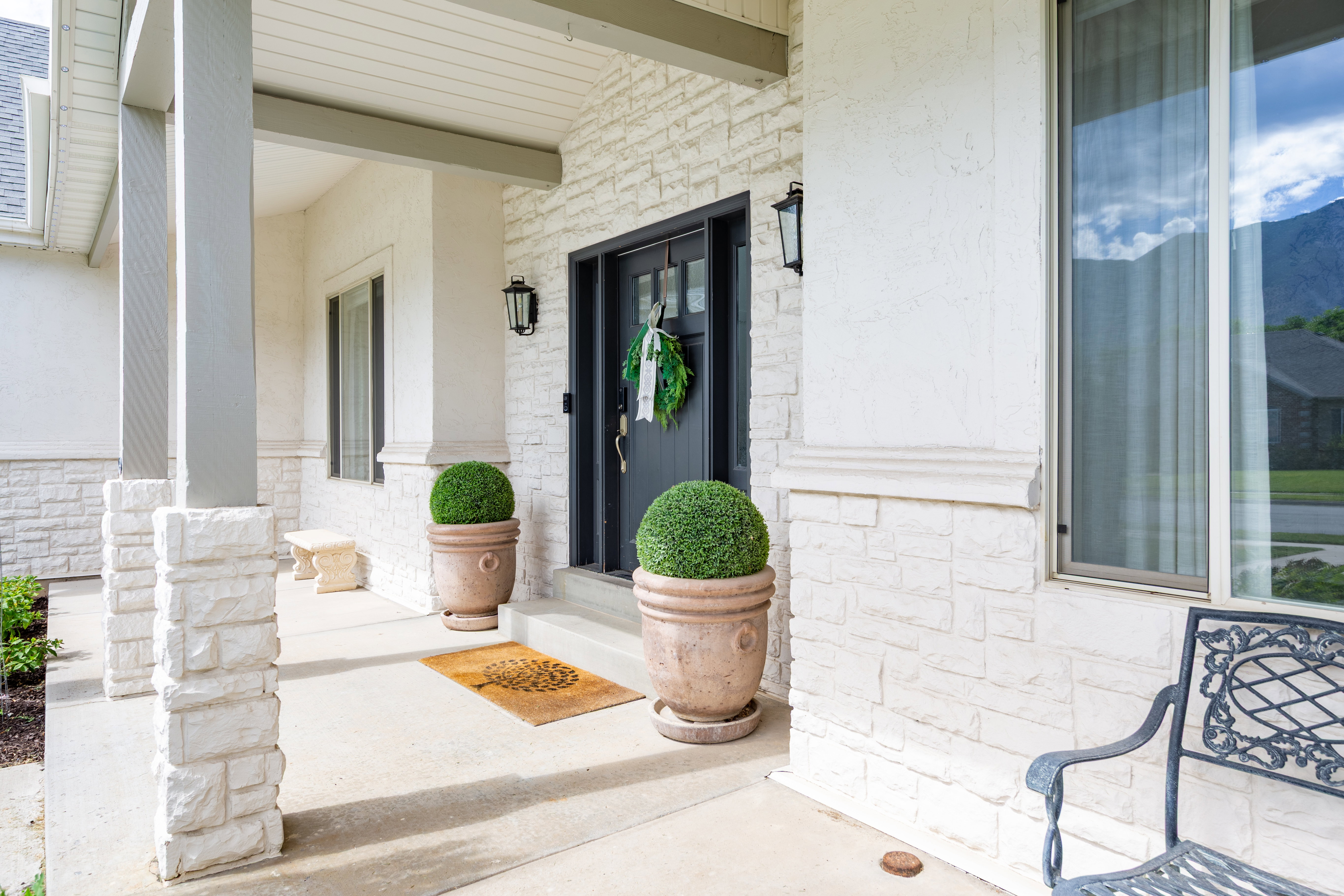 Front entry featuring a dark-paneled door with opaque glass details, white stacked stone veneer, textured stucco siding, and a covered porch with stone-clad columns