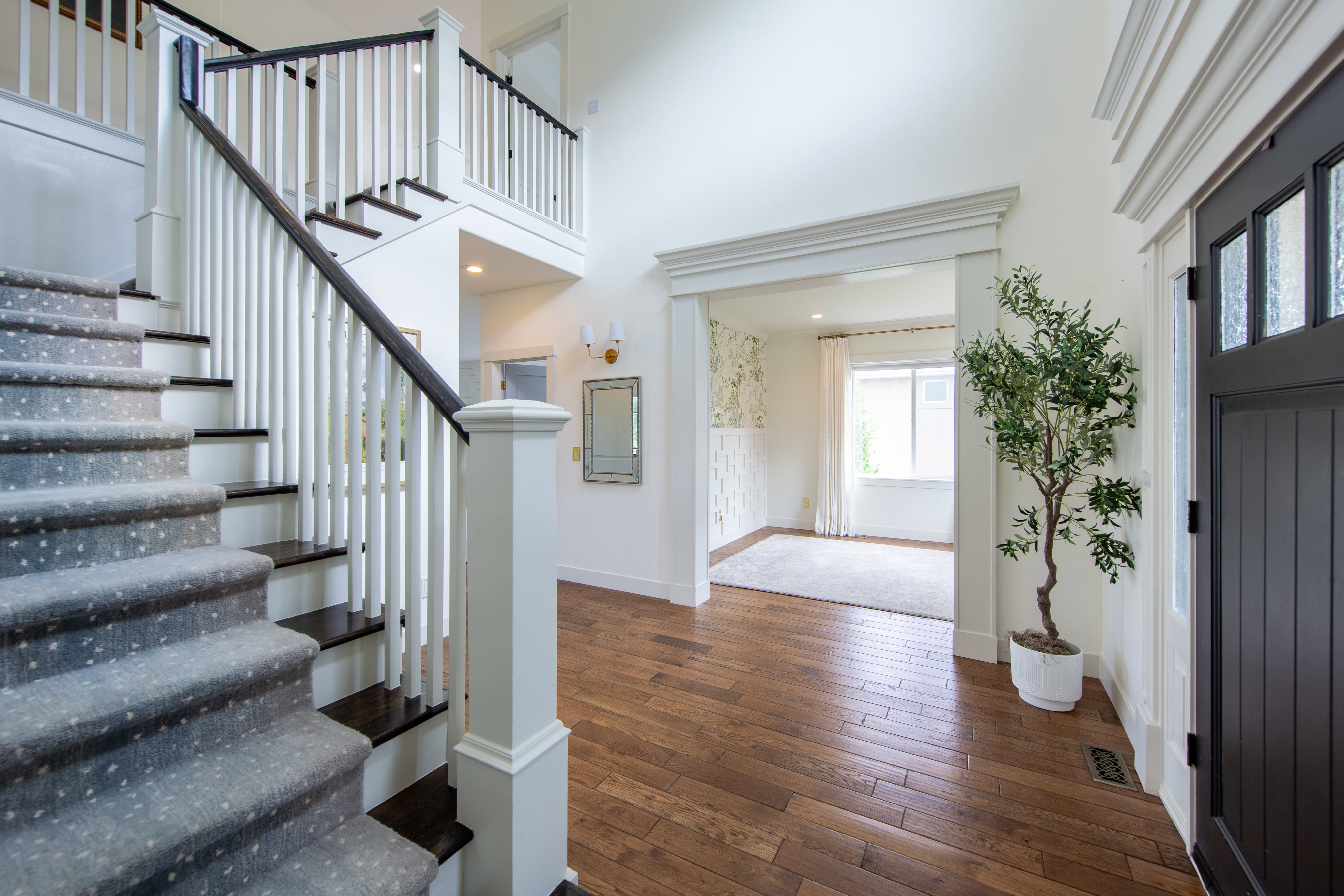 Grand entryway featuring rich wood-finish flooring, a contemporary staircase with dark treads and white risers, and a prominent front door with multiple glass lites