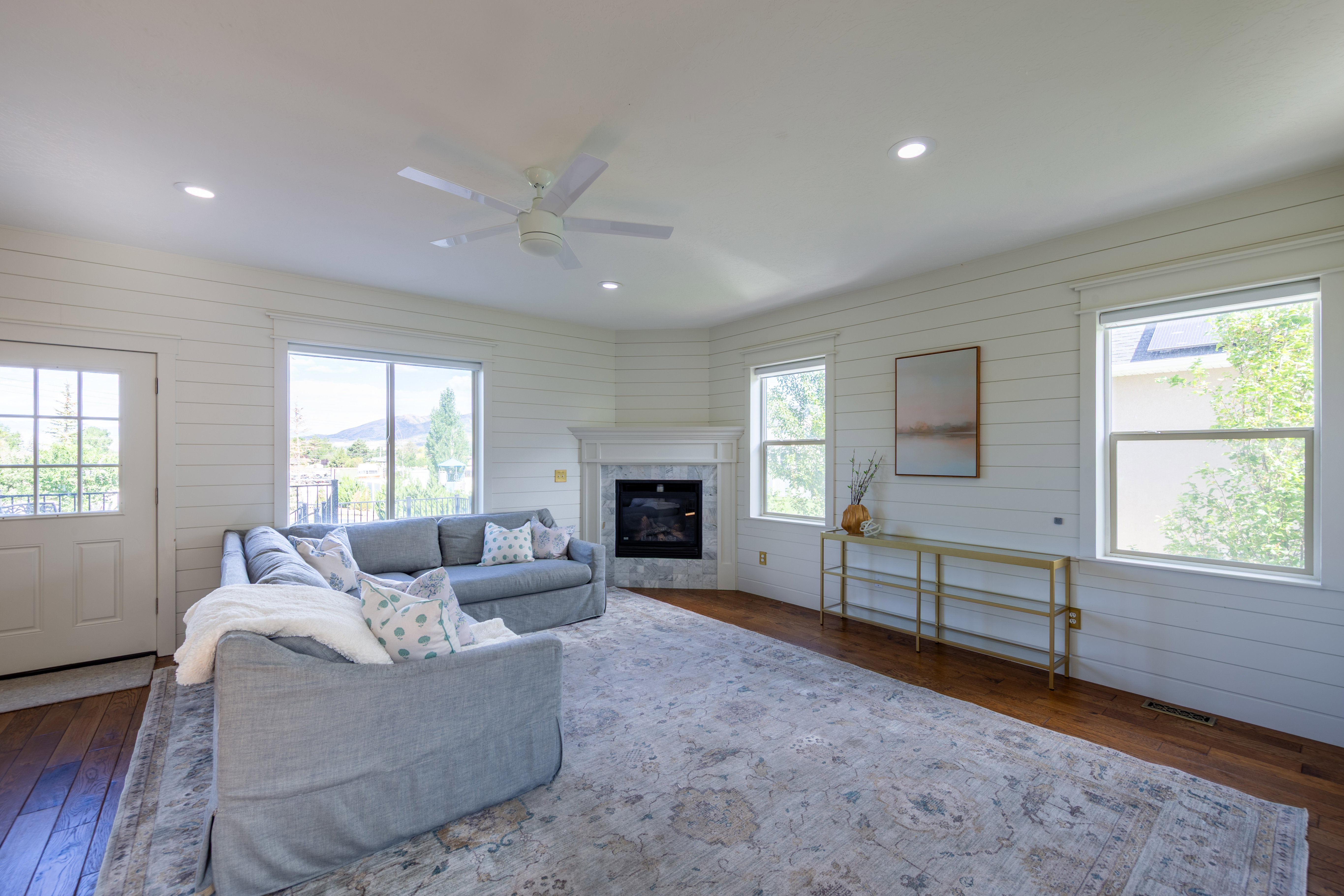 Spacious room featuring wood-finish flooring, white shiplap walls, multiple windows, recessed lighting, and a white ceiling fan