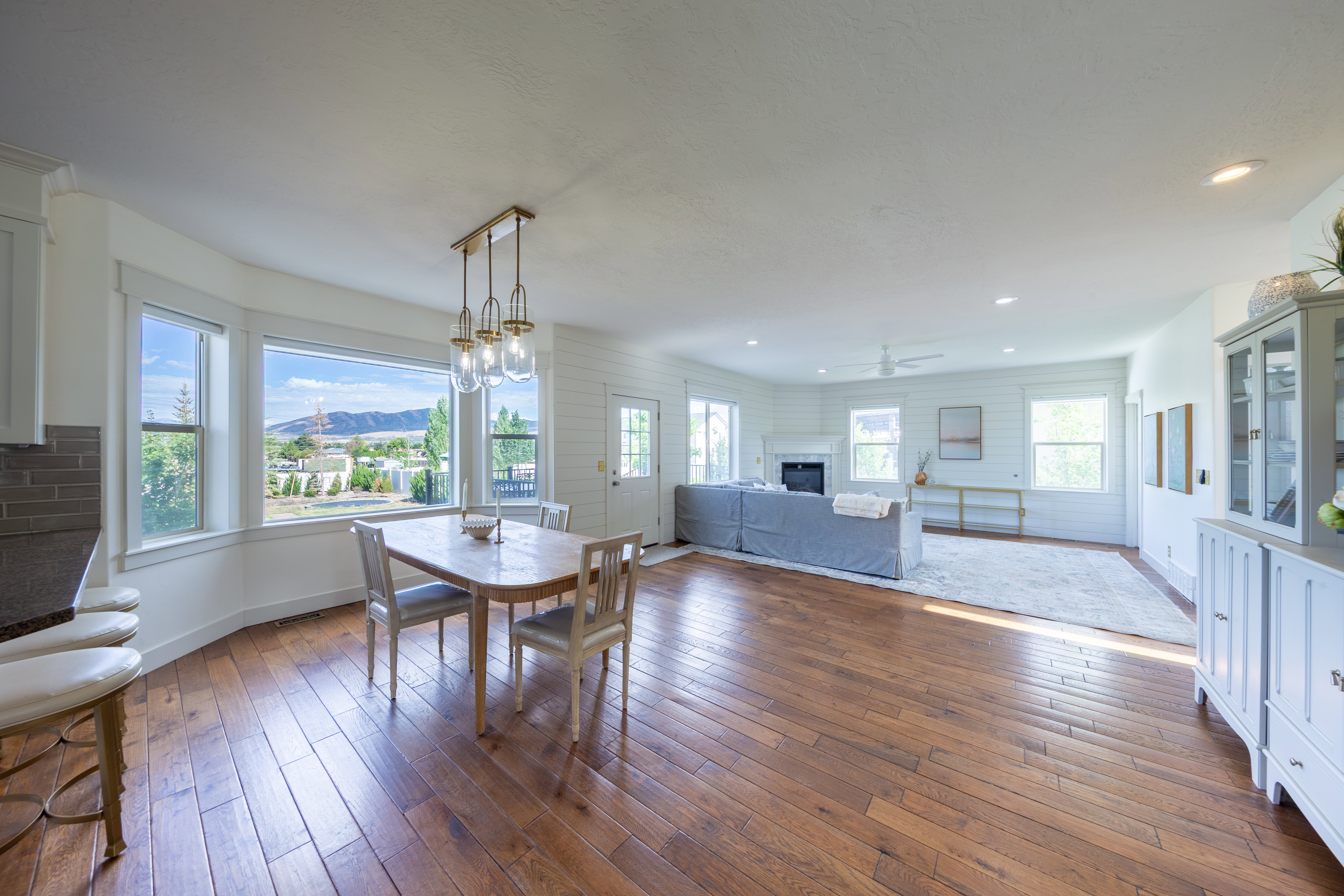 Open-concept living area featuring wood-finish flooring, a dining space with a multi-light pendant fixture, and a bay window