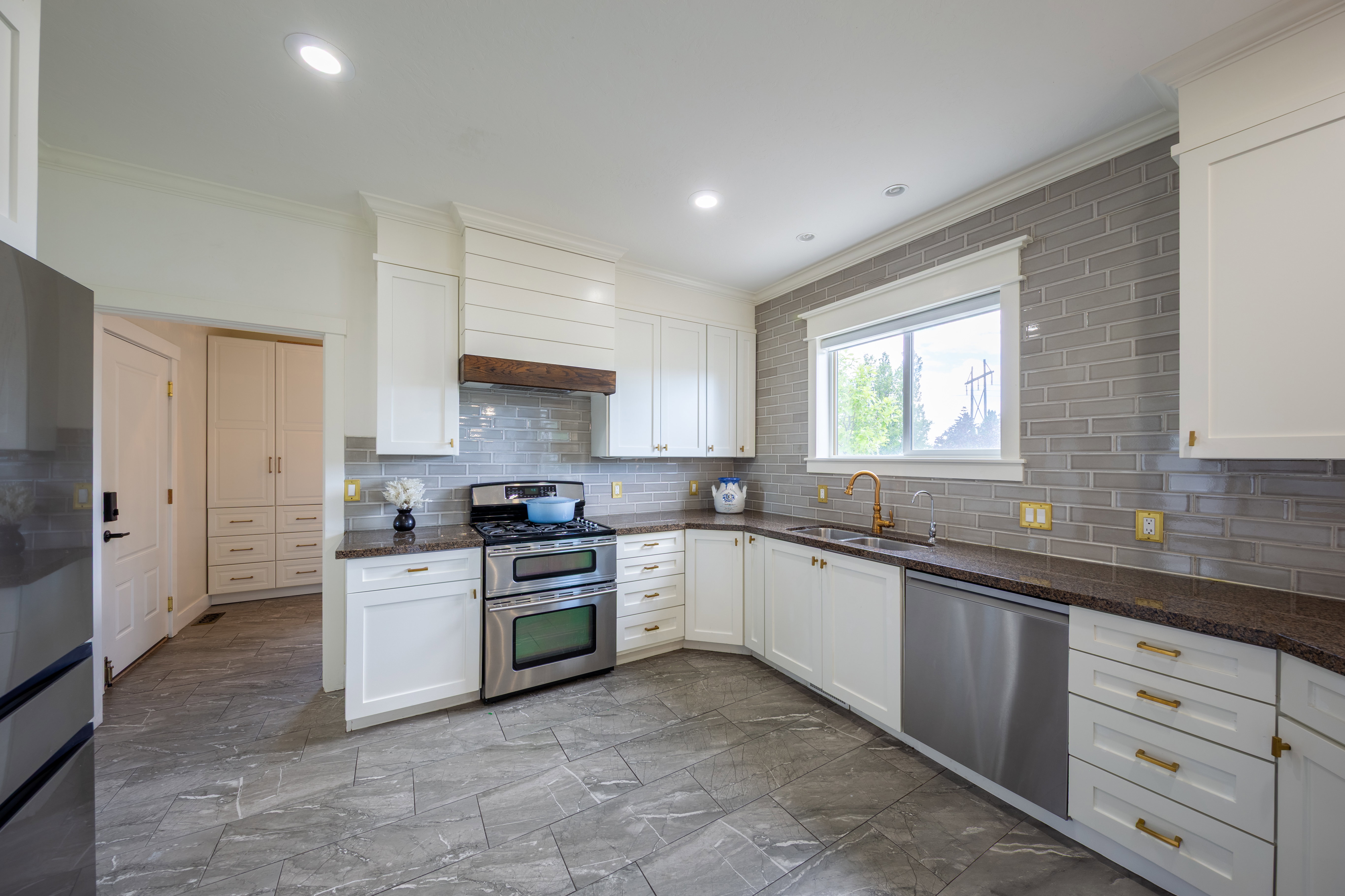 Kitchen featuring white cabinetry with gold-toned hardware, dark stone countertops, and a gray subway tile backsplash