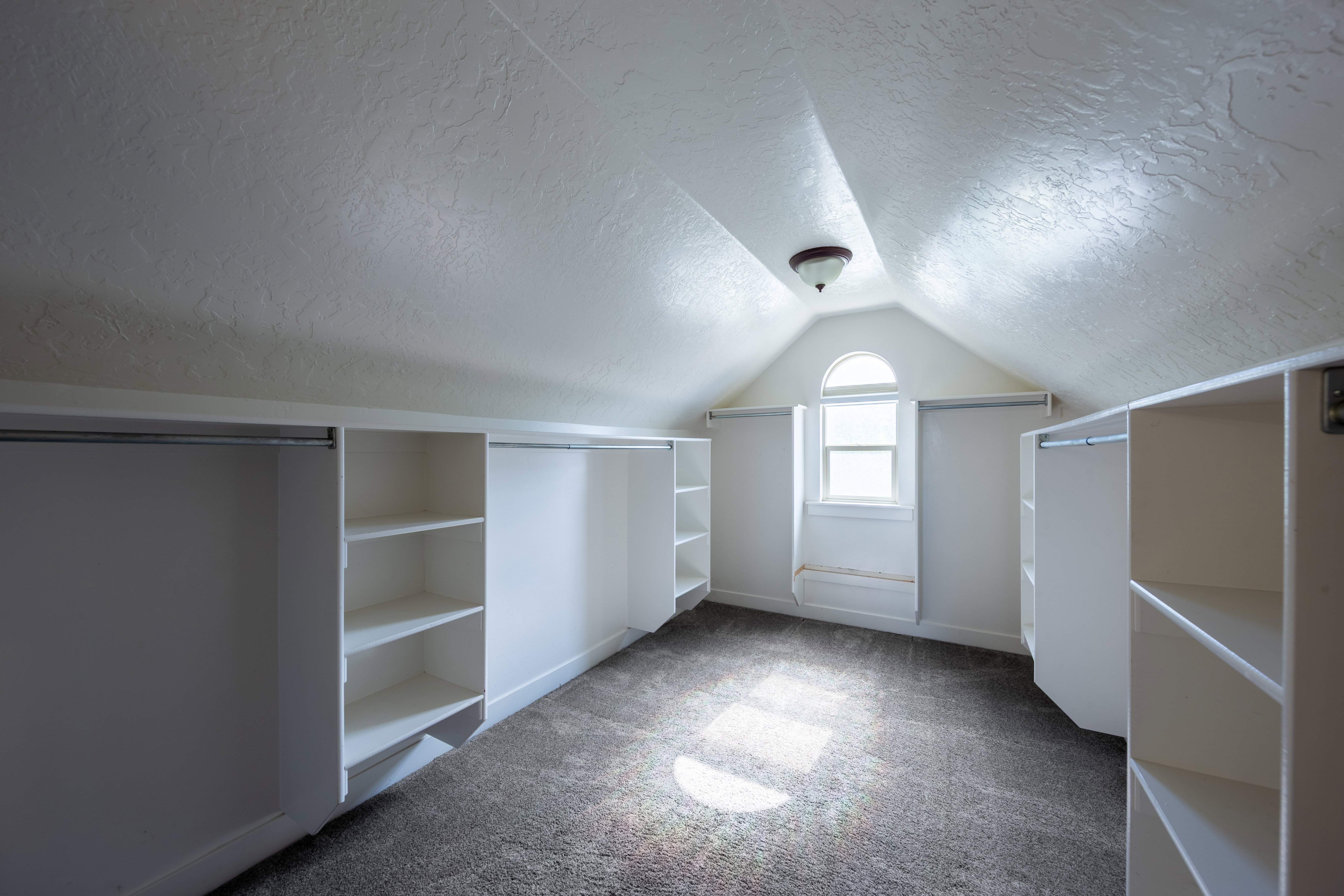 Attic space featuring sloped ceilings, a vaulted window, and recessed shelving