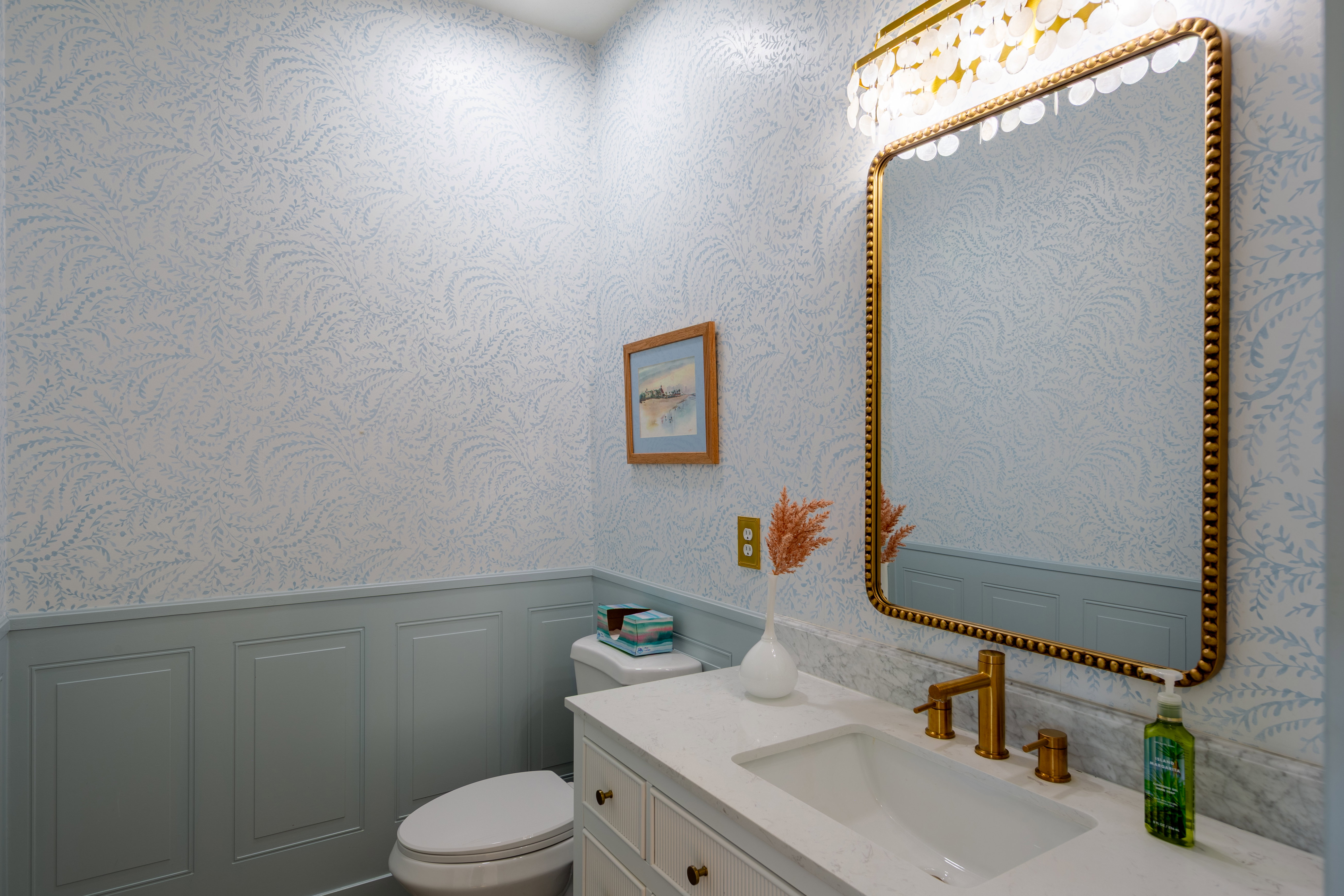 Powder room featuring a vanity with a white countertop and integrated sink, gold-toned faucet, and a gold-framed mirror