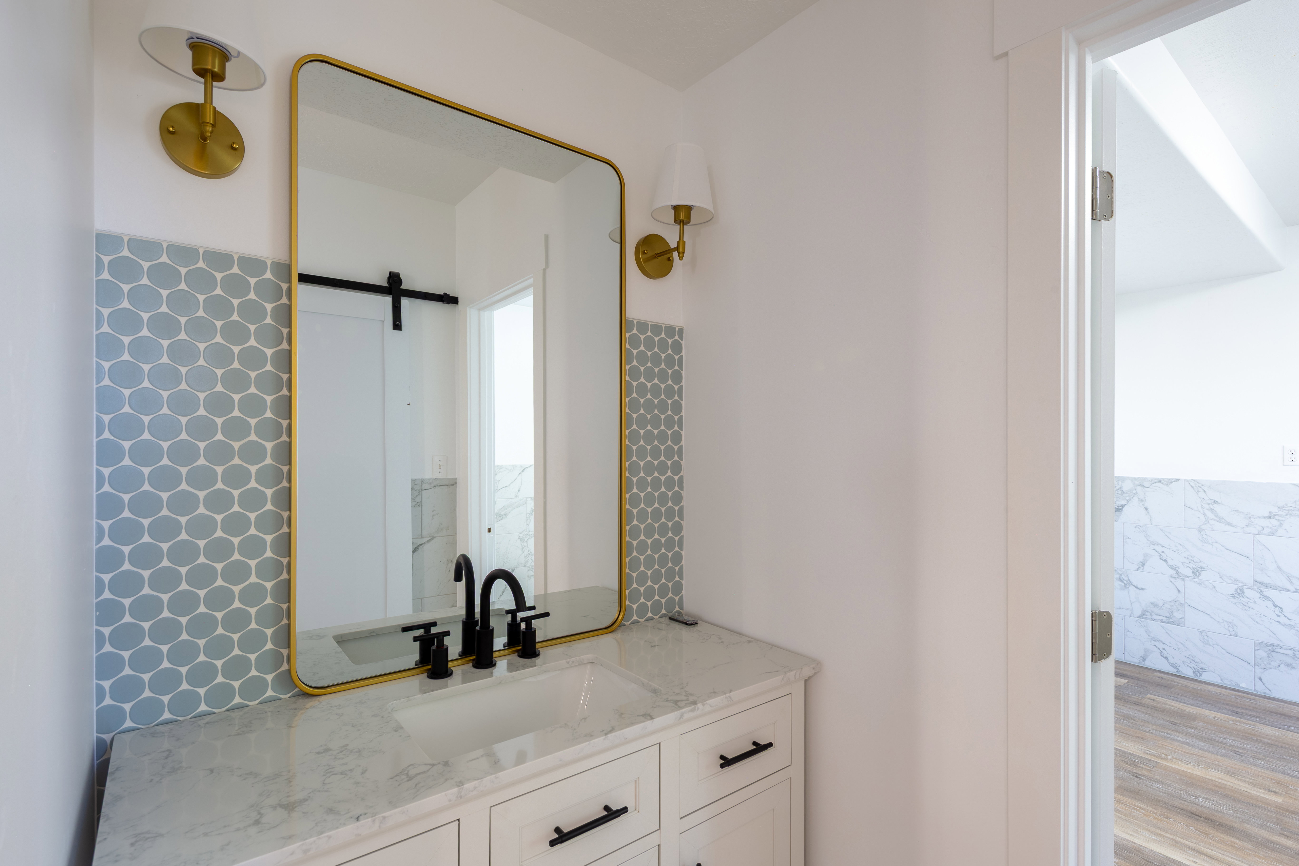 Vanity featuring a gold-framed mirror, dual brass sconces, hexagon tile backsplash, and a white countertop with an integrated sink