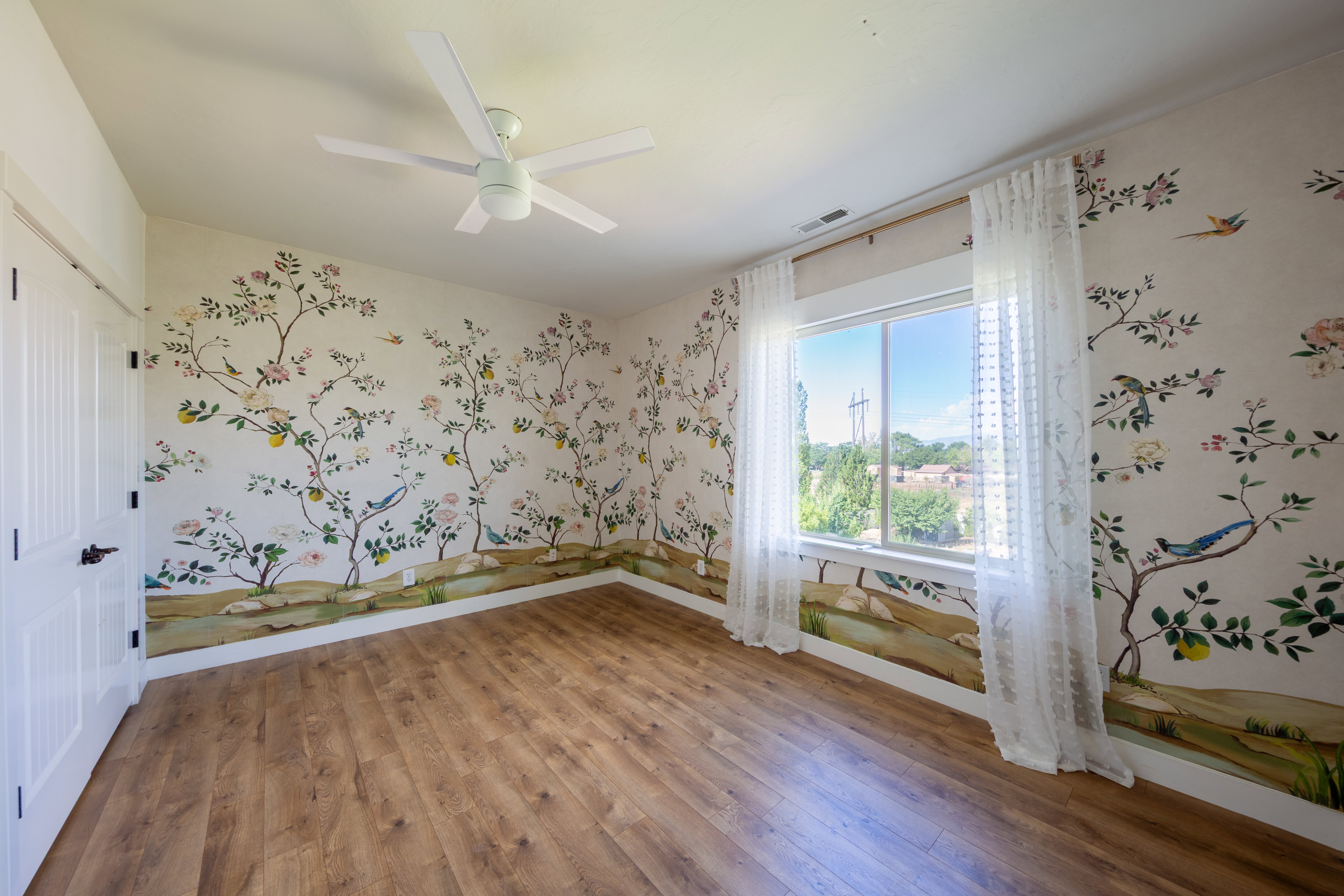 Spacious room featuring wood-finish flooring, a contemporary ceiling fan, and decorative wall murals