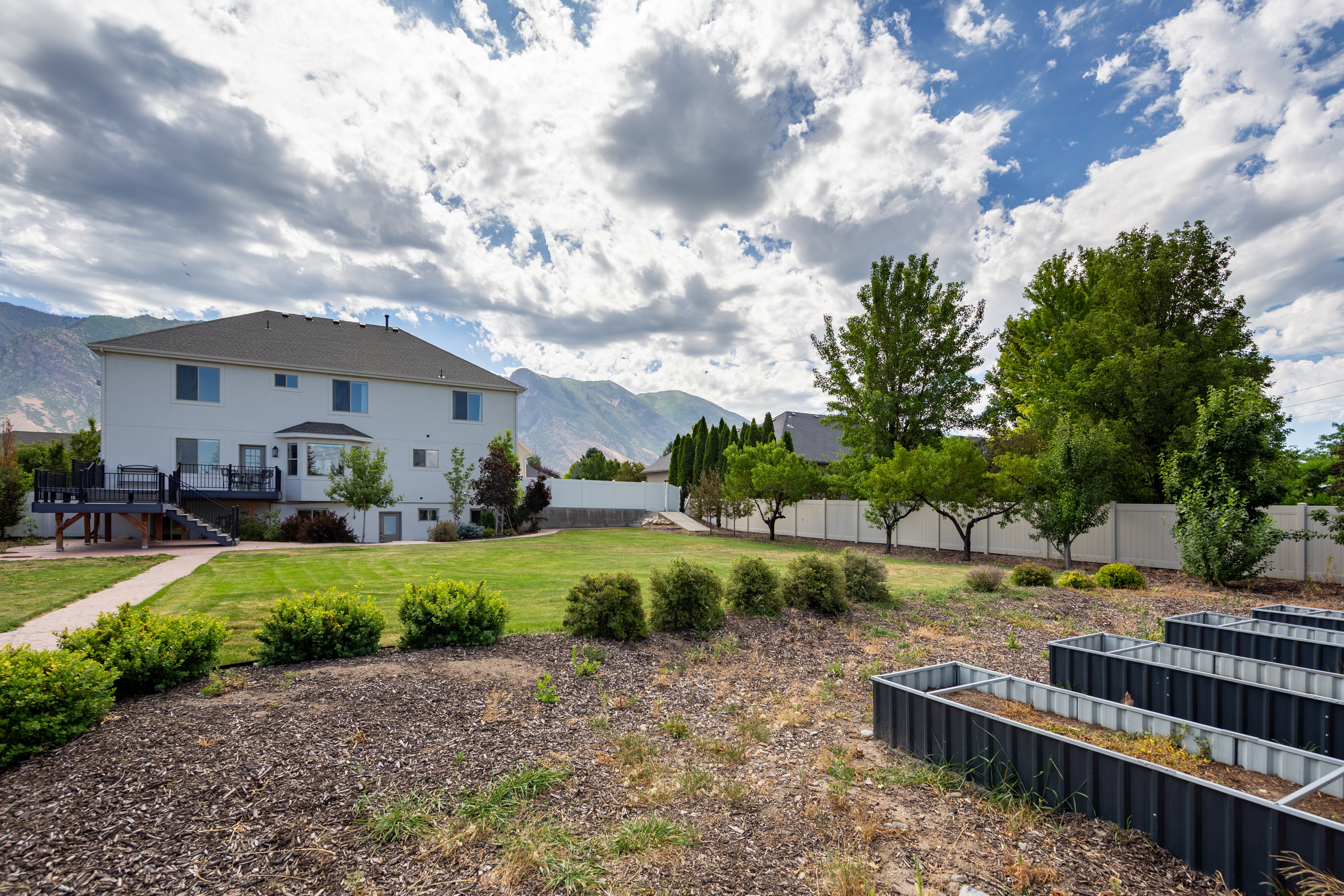 Expansive backyard featuring a large green lawn, mature trees, and a concrete paver pathway