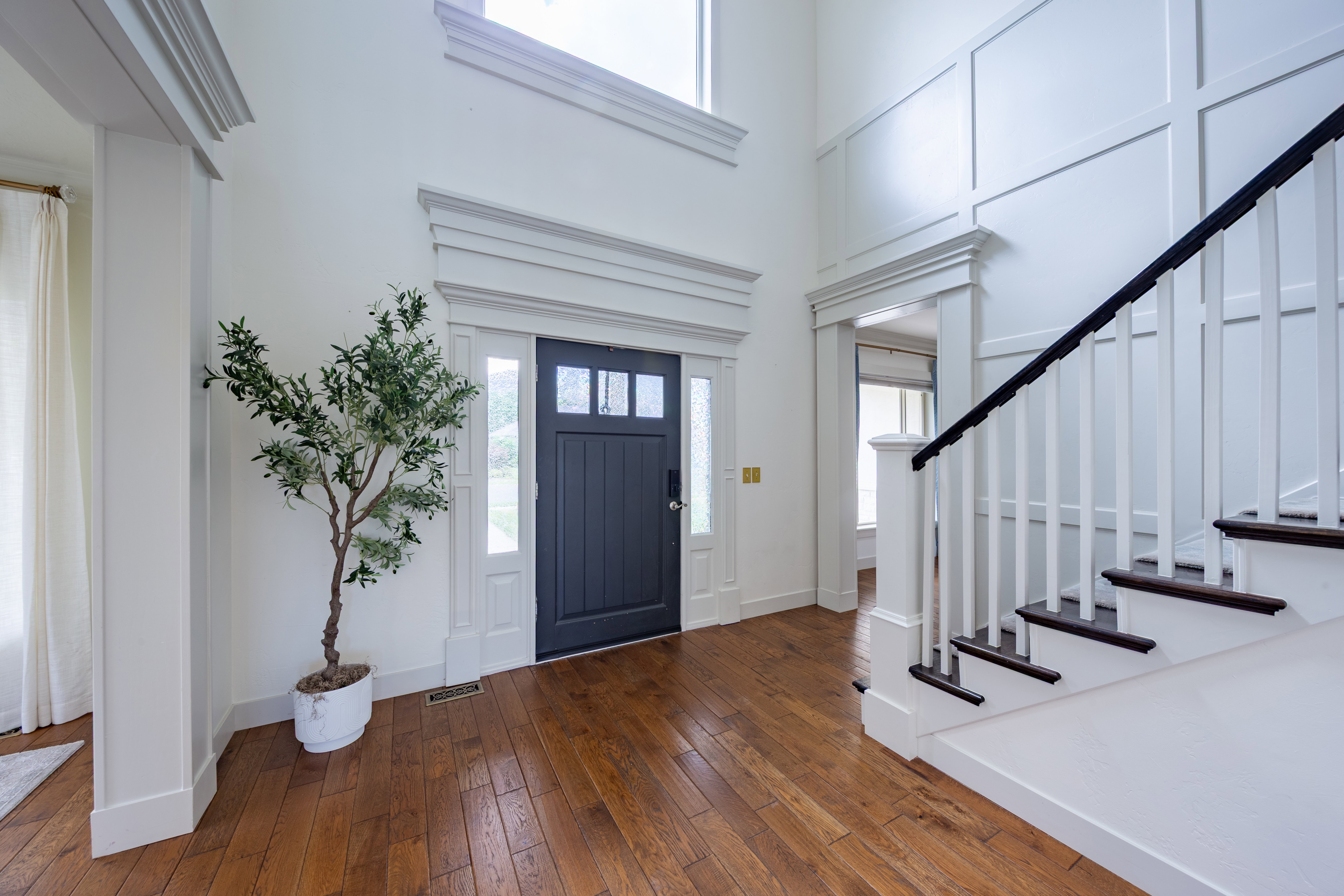 Entry foyer featuring wood-finish flooring, a dark-paneled door with sidelights, and a grand staircase with dark treads and white risers