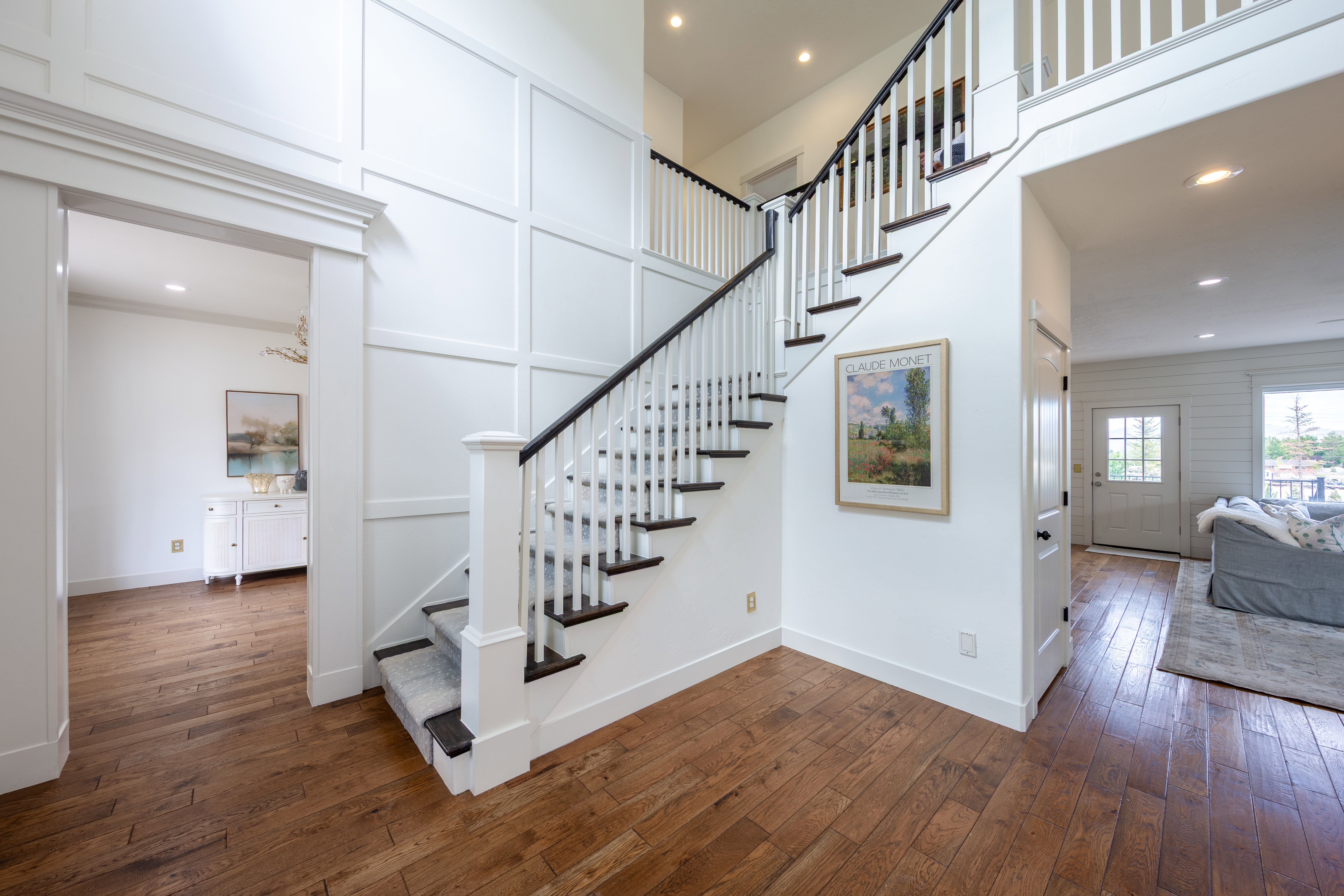 Two-story foyer featuring wood-finish flooring, a white staircase with dark treads and handrail, and board and batten wall paneling