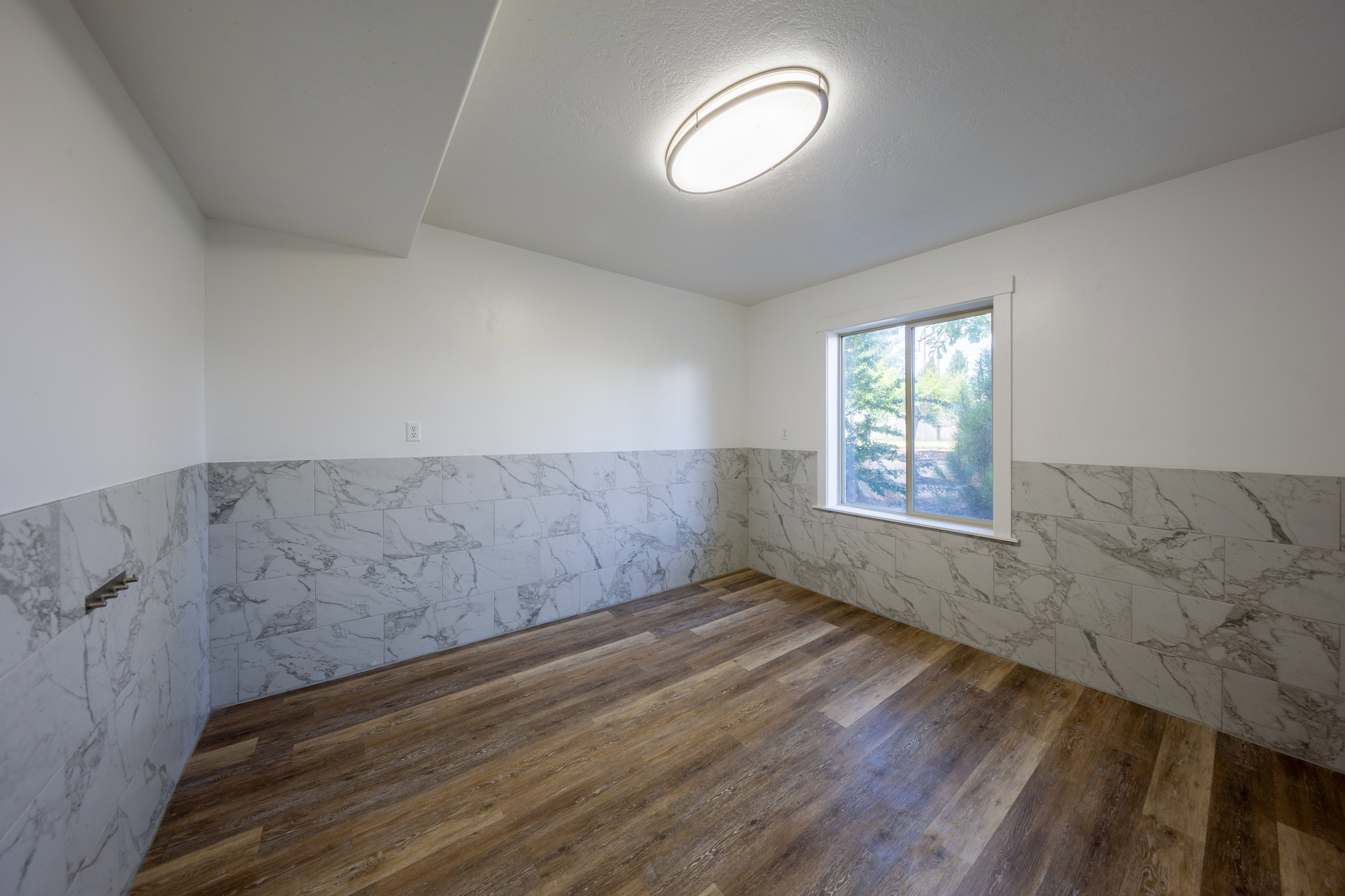 Room featuring wood-finish flooring, white walls, and a window providing natural light