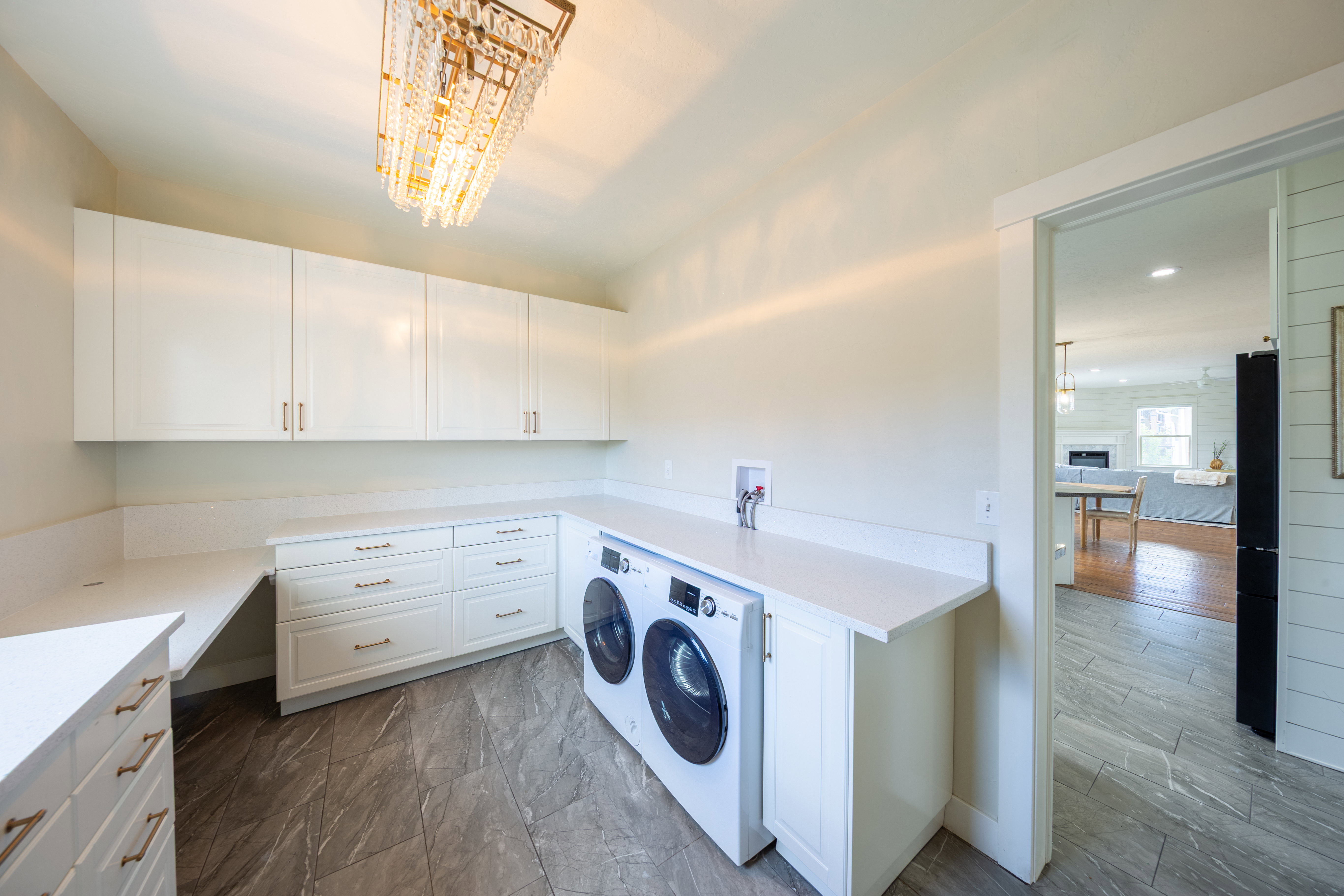 Dedicated laundry area featuring a modern chandelier, extensive white cabinetry, light-toned countertops, and durable tile flooring