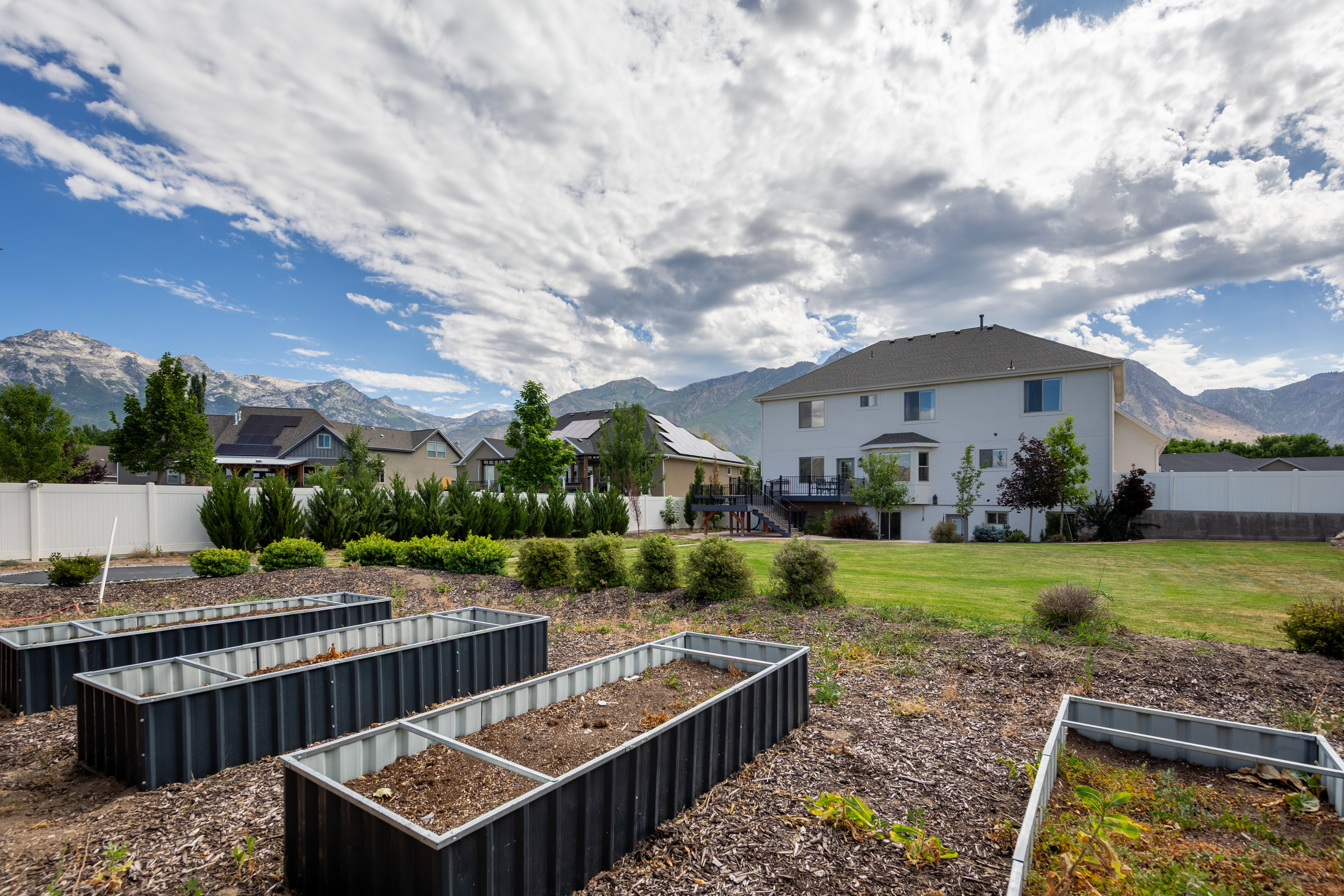 Expansive backyard featuring multiple raised garden beds, a spacious lawn area, and a white privacy fence