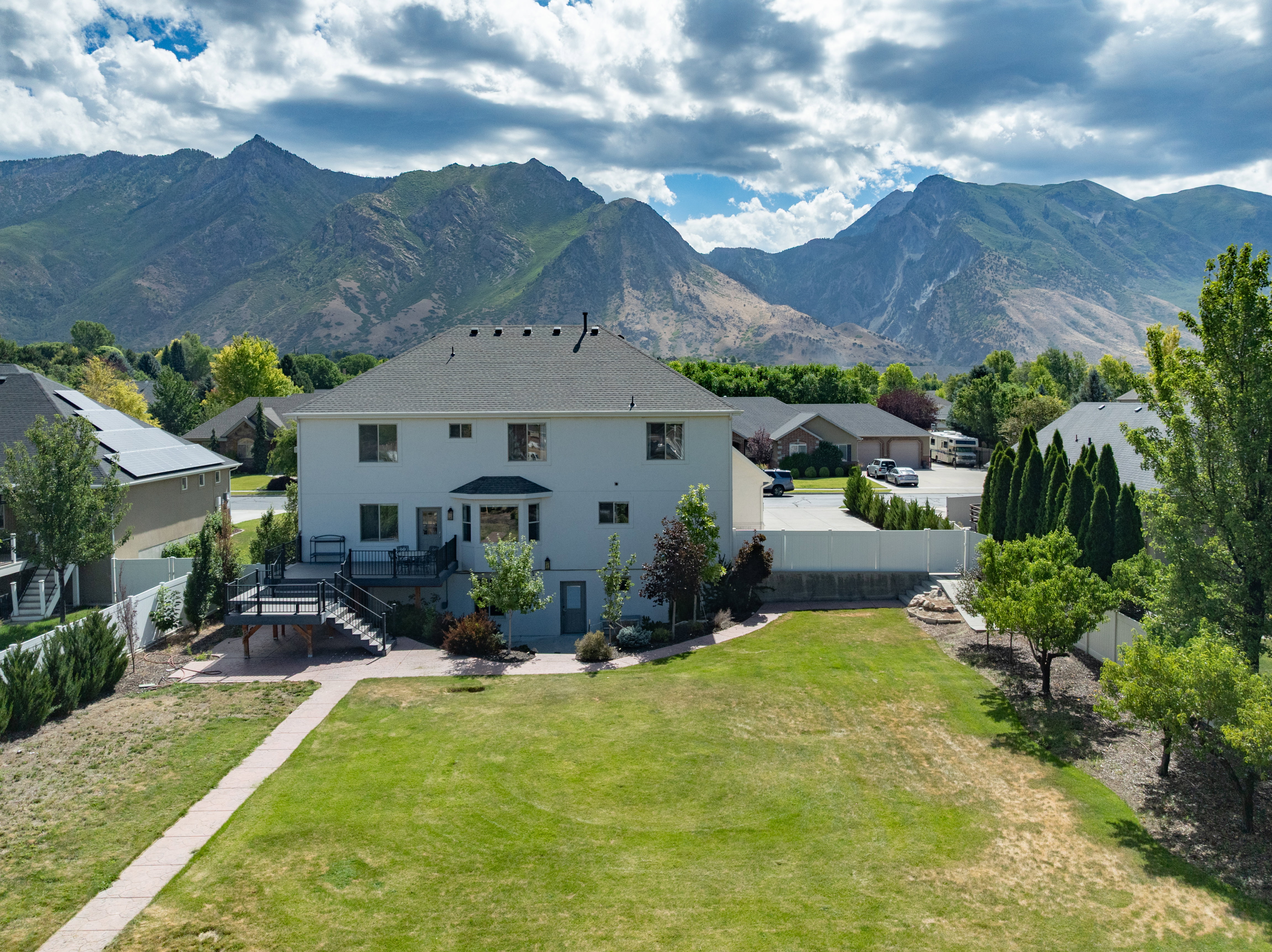Expansive backyard featuring a large green lawn, concrete paver pathway, and mature trees