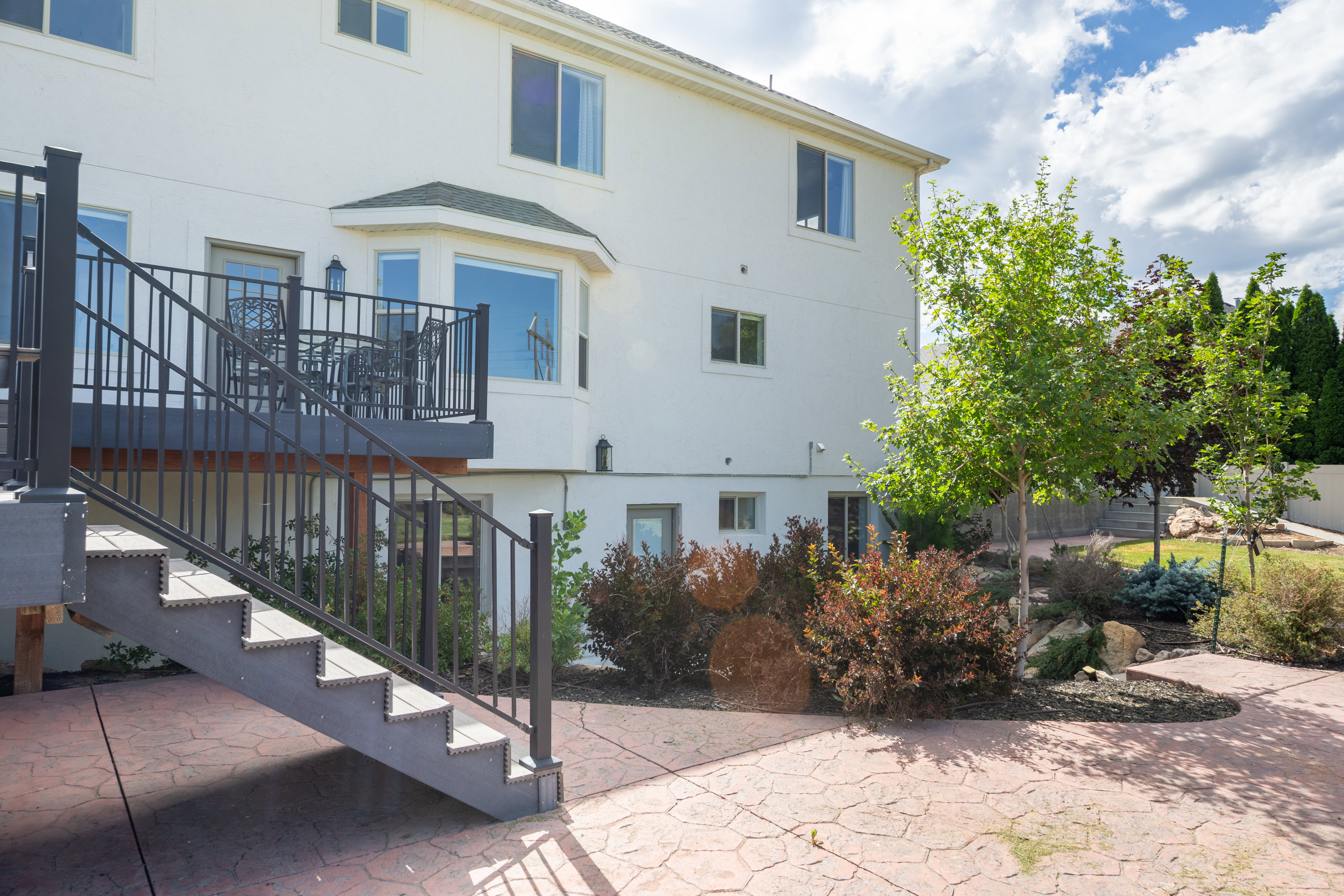 Rear exterior featuring a composite deck with metal railings and stairs, a bay window, and a stamped concrete patio