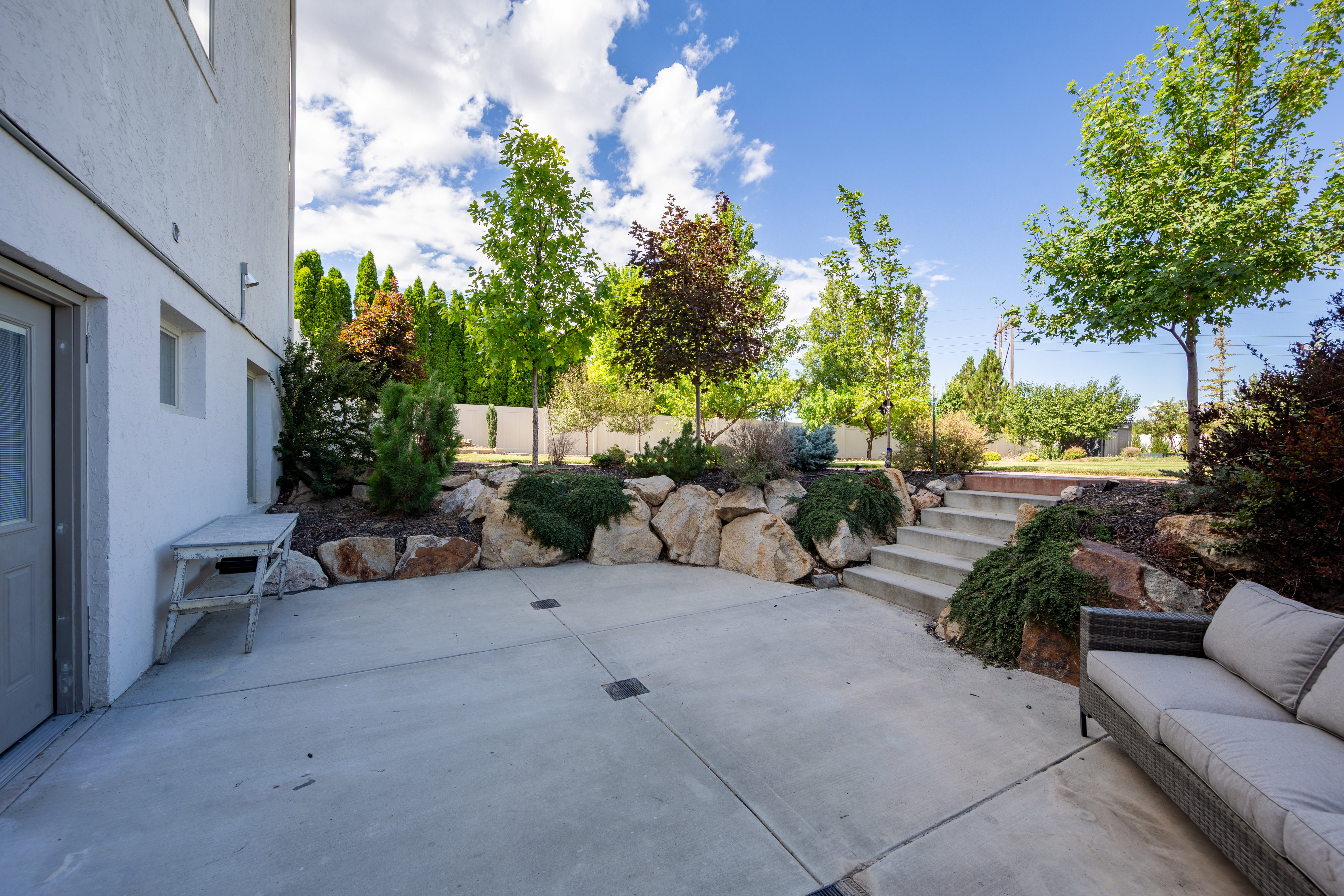 Spacious concrete patio with tiered landscaping and mature trees